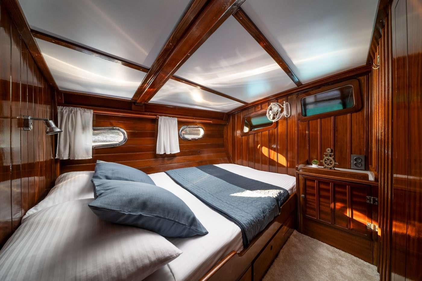 yacht cabin interior with double bed, blue pillows, wooden paneling and portholes