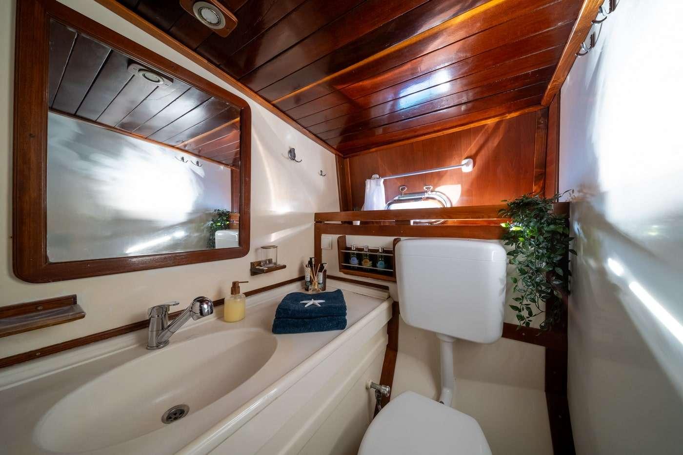 yacht bathroom interior with white sink, wood-framed mirror, toilet and wood ceiling