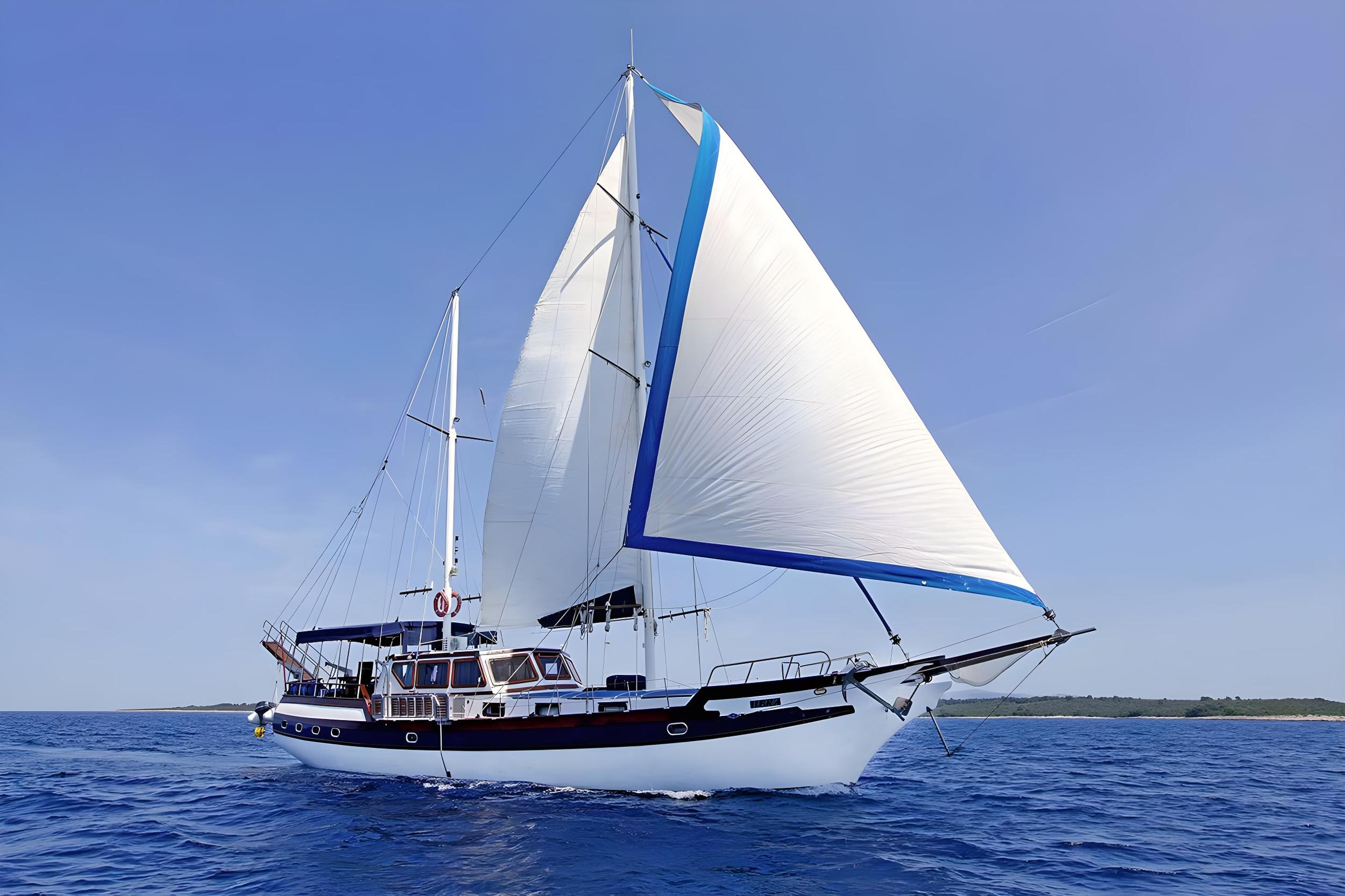 Traditional wooden gulet sailing underway with large white mainsail and blue-trimmed furled headsail