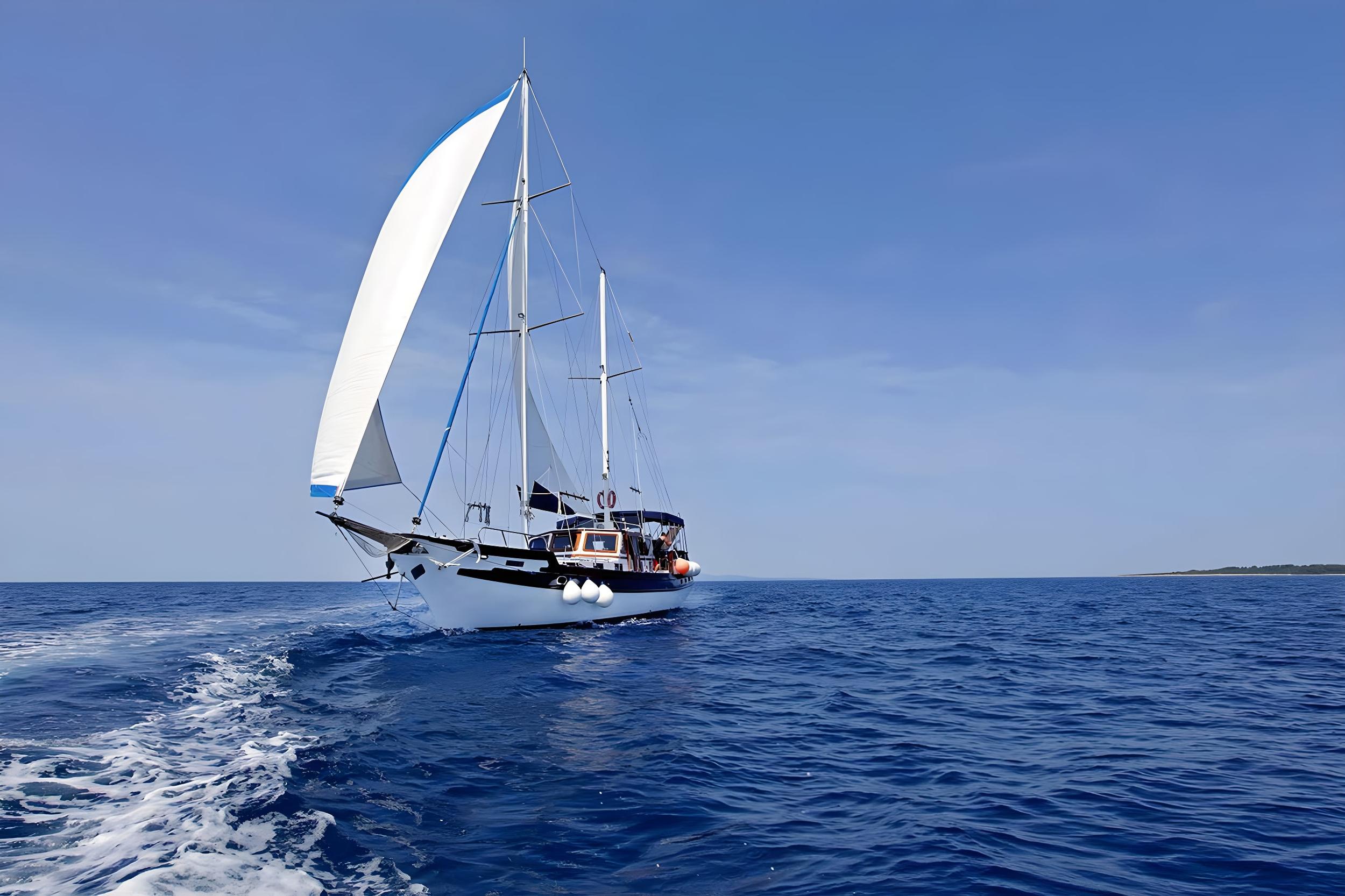 Classic two-masted gulet sailing under full white sails on deep blue Mediterranean sea