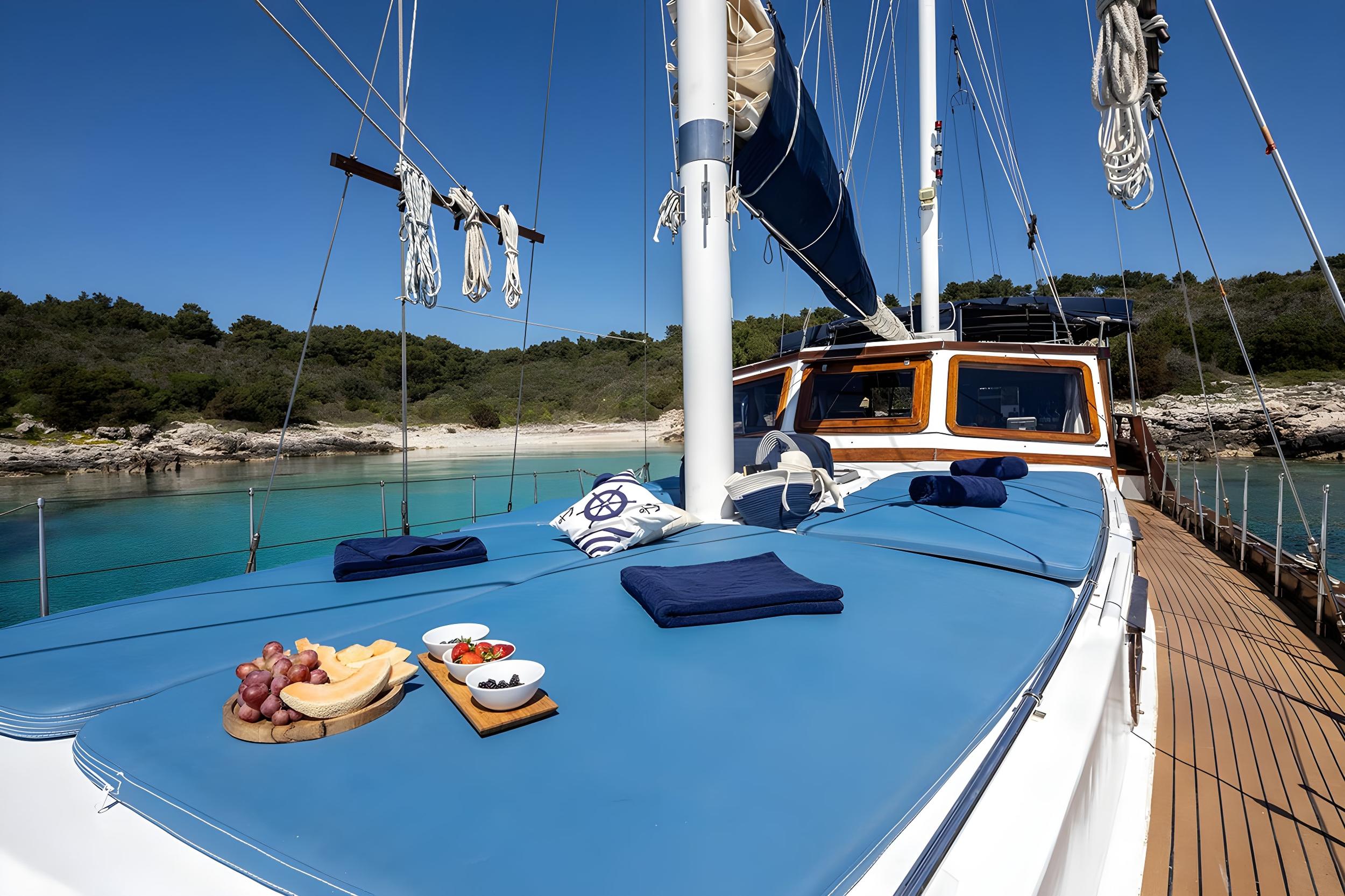 Gulet bow deck with blue cushions, folded navy towels, and fresh fruit and berry snack boards served on teak