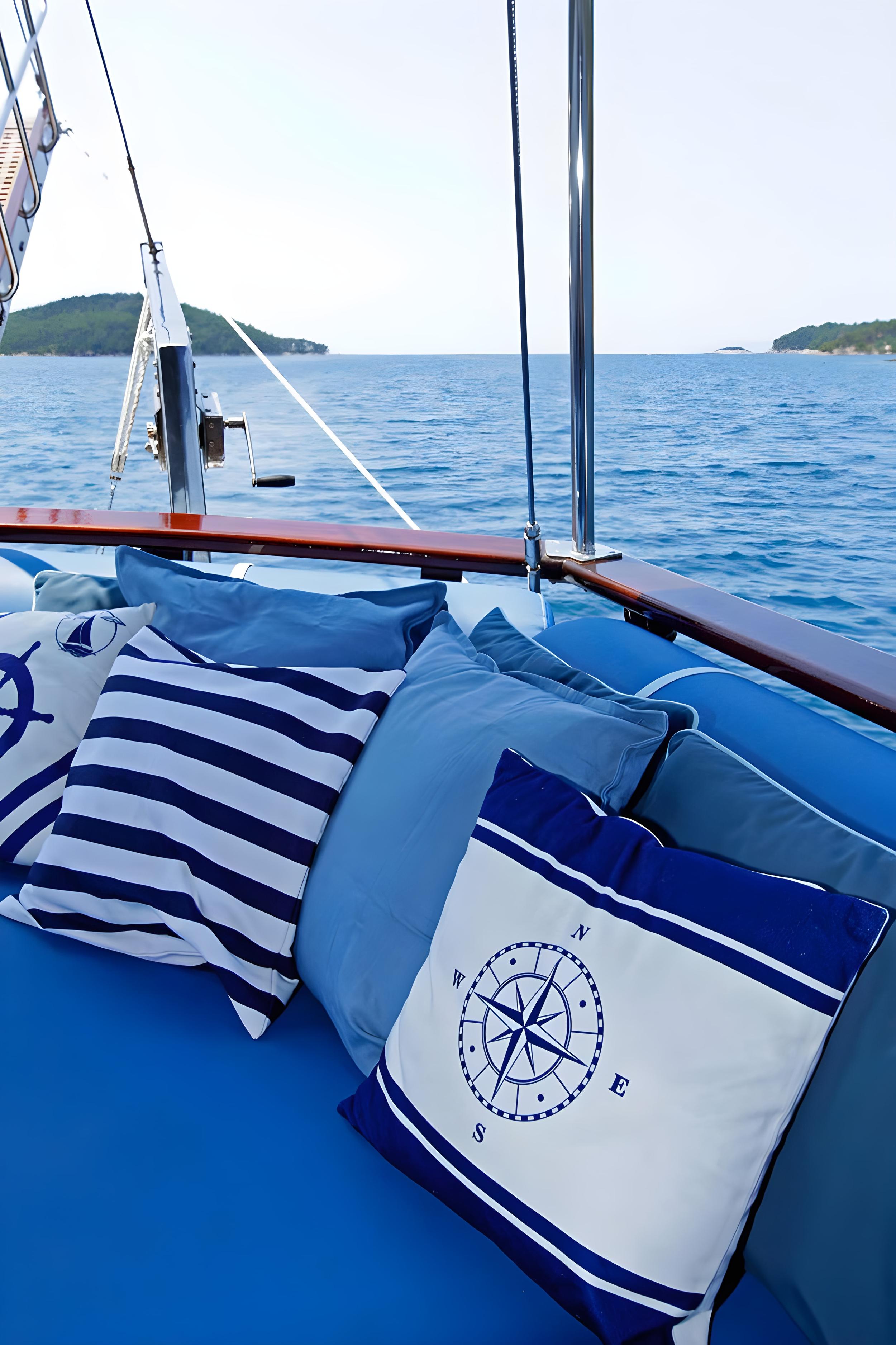 gulet foredeck blue cushioned seating with nautical stripe and compass rose pillows overlooking calm sea and wooded islands