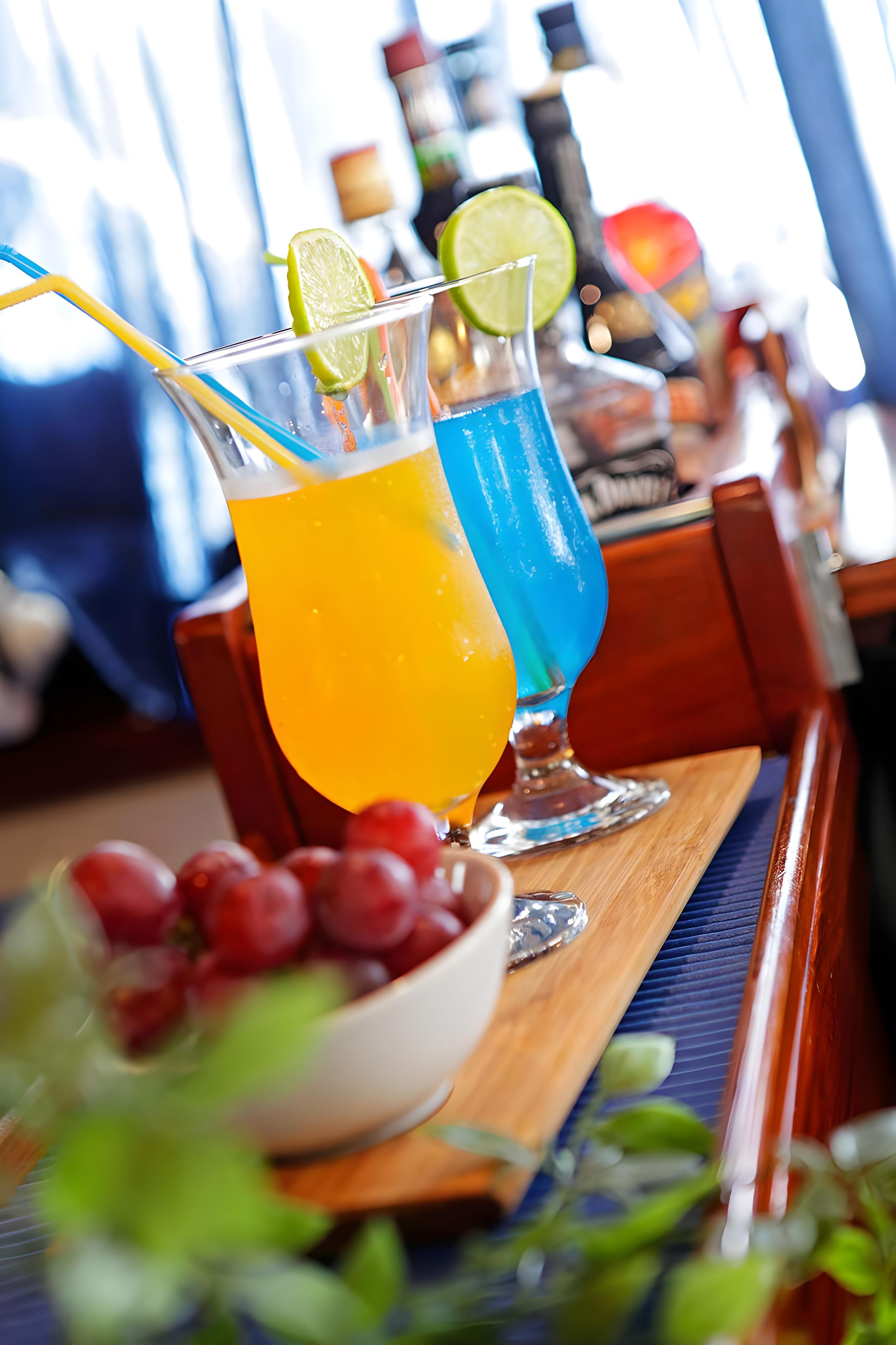 orange and blue cocktails with lime garnish on yacht bar with spirit bottles behind