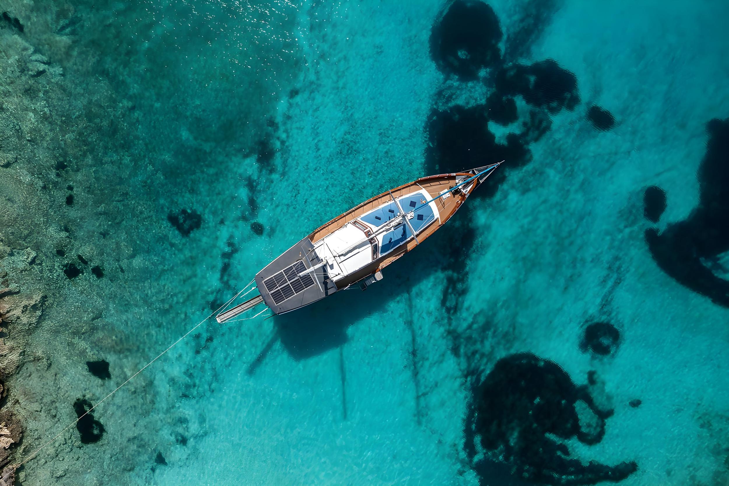 aerial drone view of traditional wooden gulet anchored in turquoise water with solar panels visible on deck