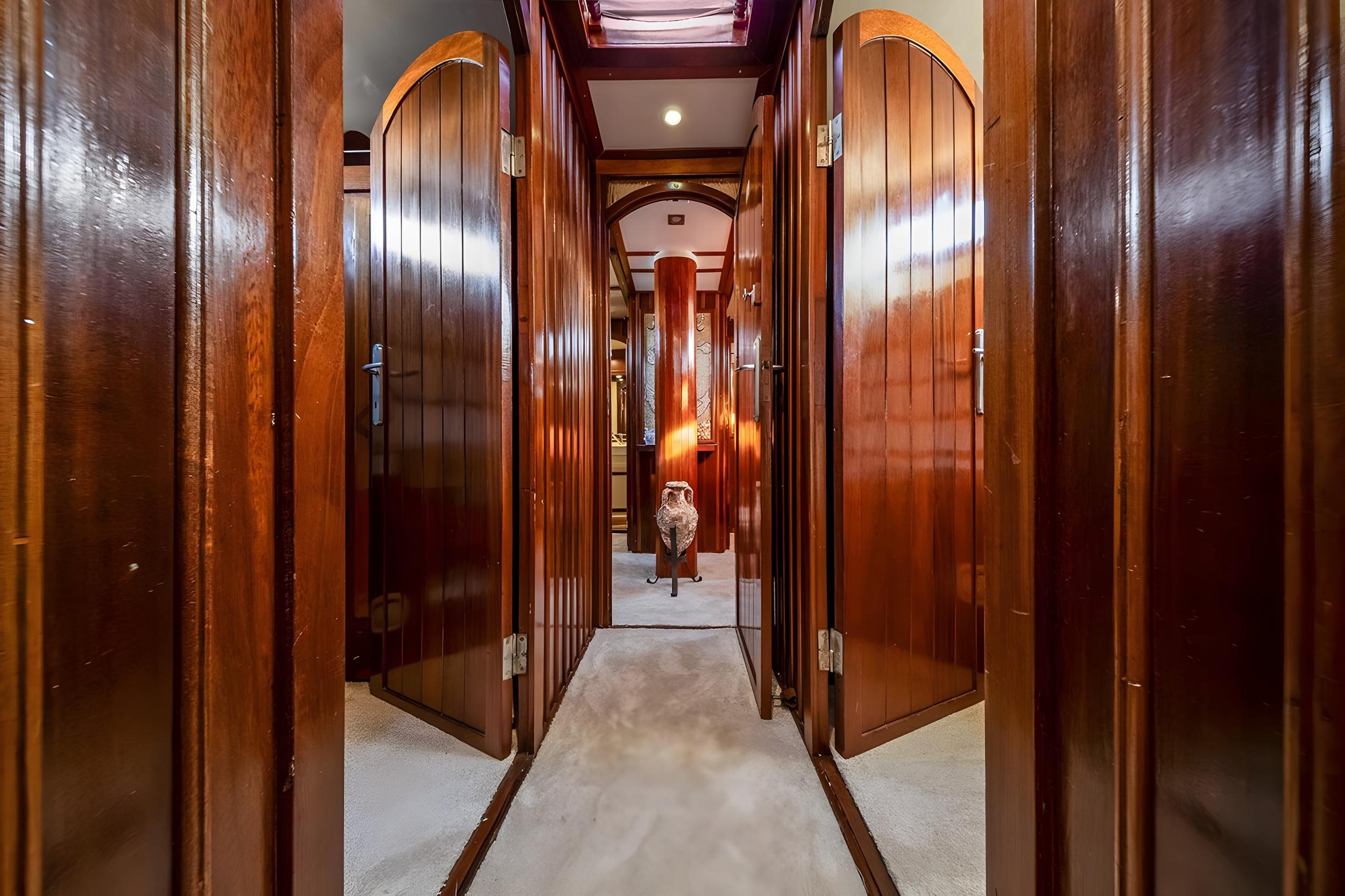 Polished mahogany interior corridor with arched cabin doors and carpeted floor on luxury gulet