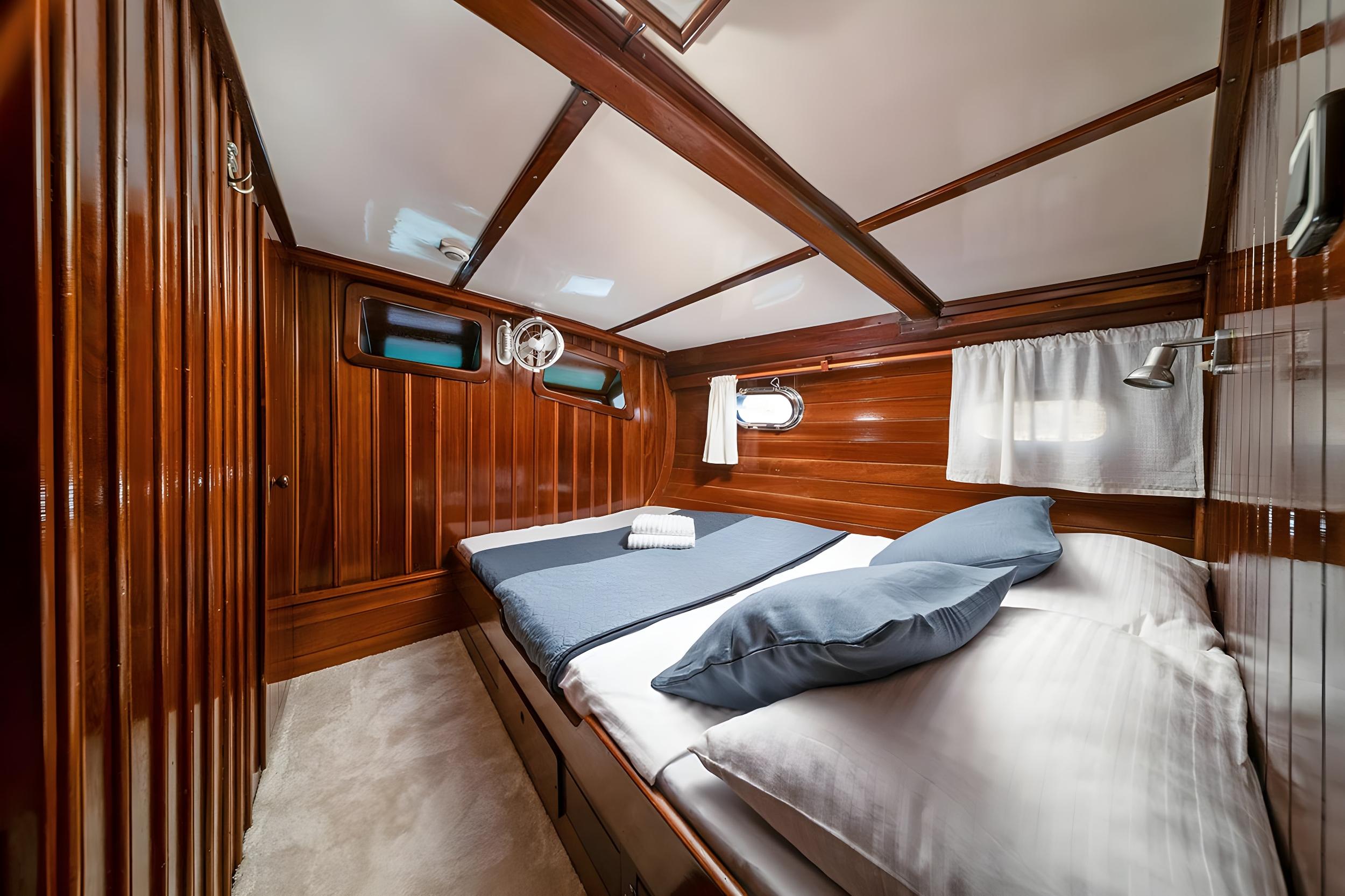 Gulet guest cabin with two single beds, blue bedding, teak wood walls and porthole windows