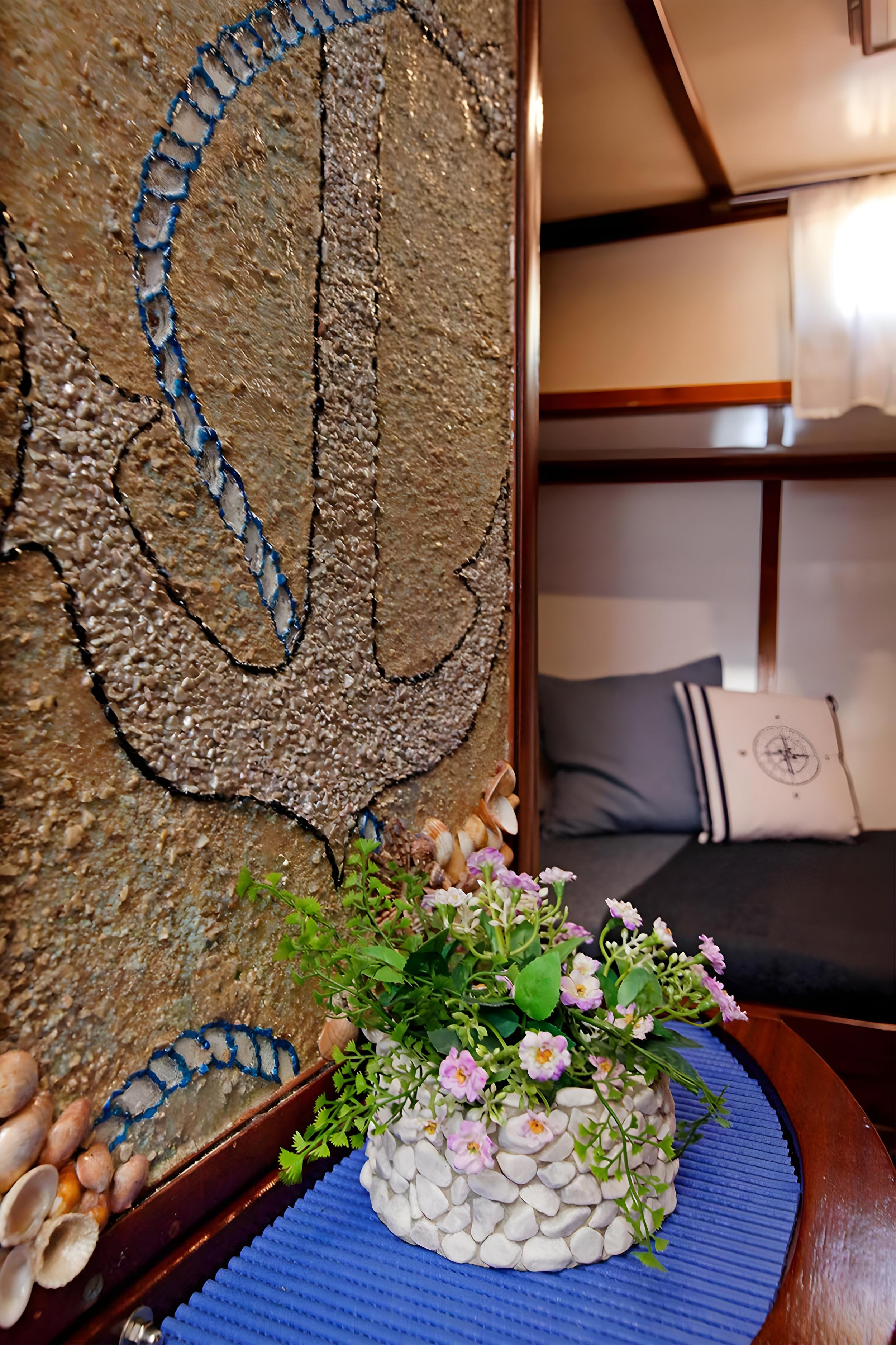 Gulet interior lounge with anchor mosaic wall art, shell decorations, compass rose cushion, and flower arrangement