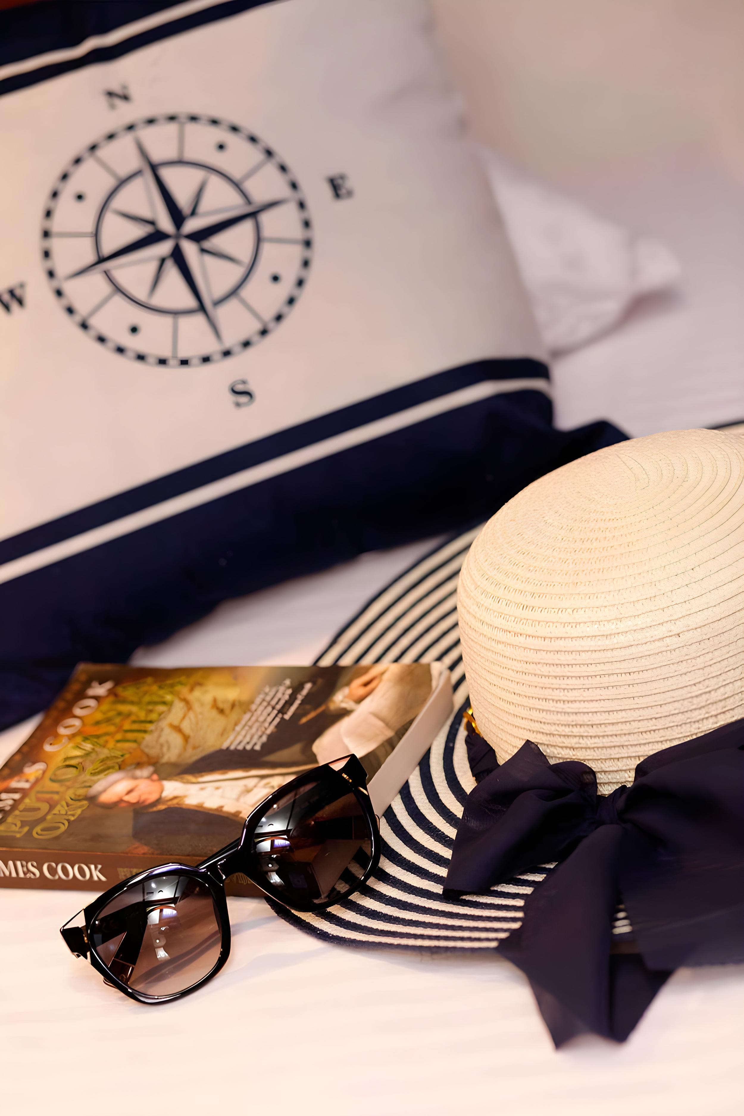 Gulet cabin bed with nautical compass pillow, straw sun hat, sunglasses, and James Cook book