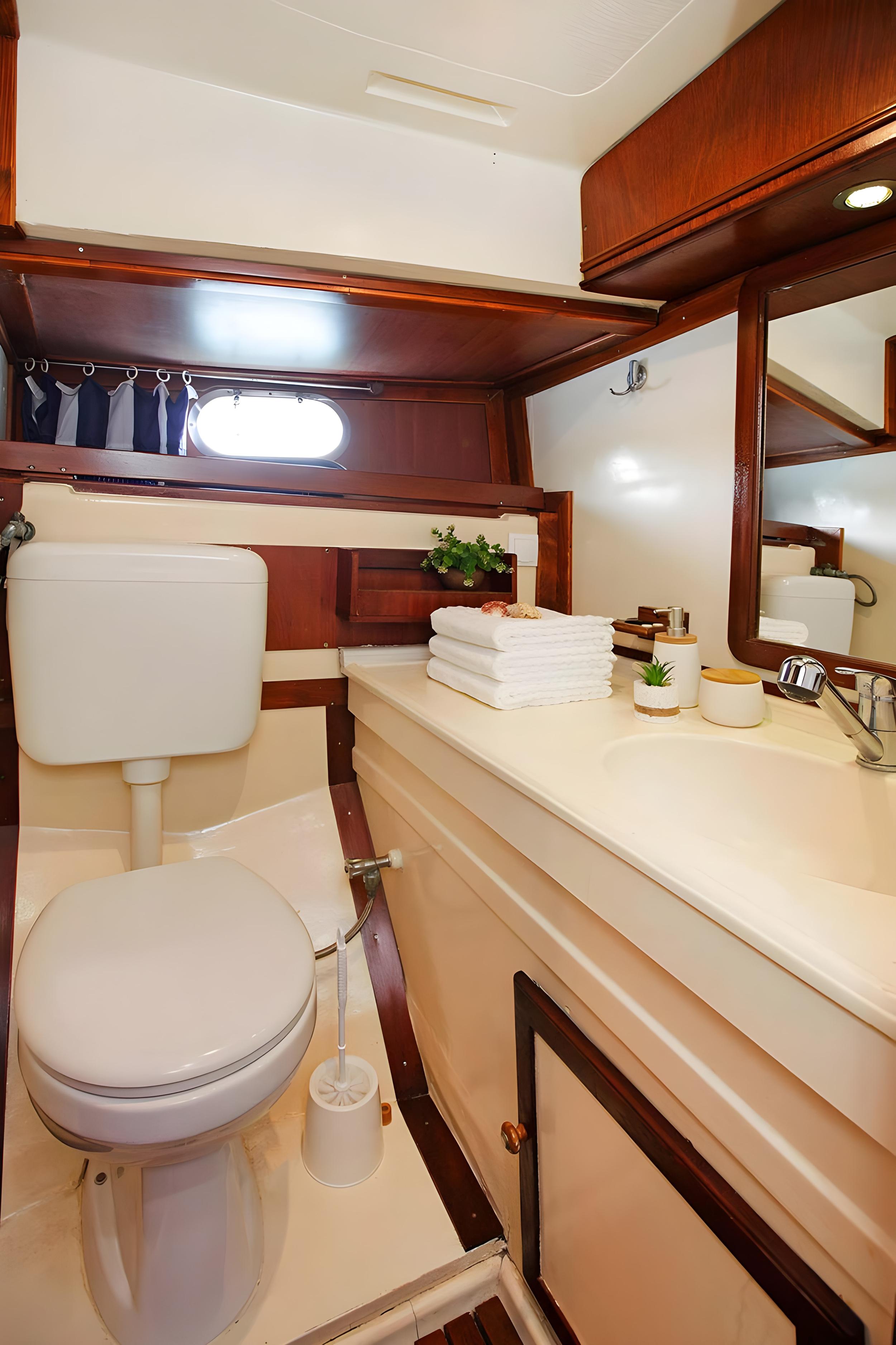 Gulet cabin en-suite bathroom with white toilet, integrated vanity basin, mirror, folded towels and oval porthole