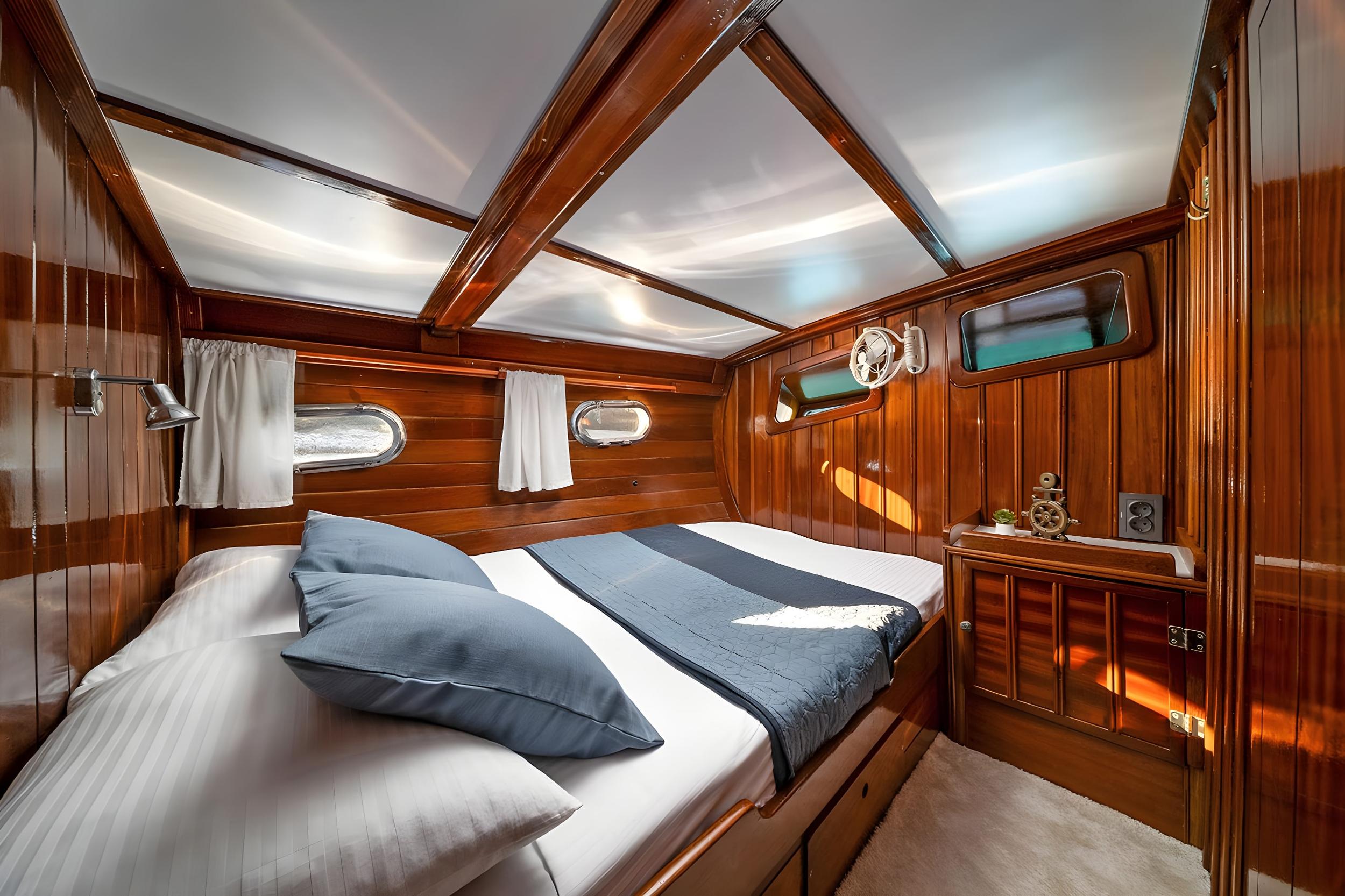 Gulet double cabin with polished mahogany walls, two oval portholes, white striped bedding and blue cushions