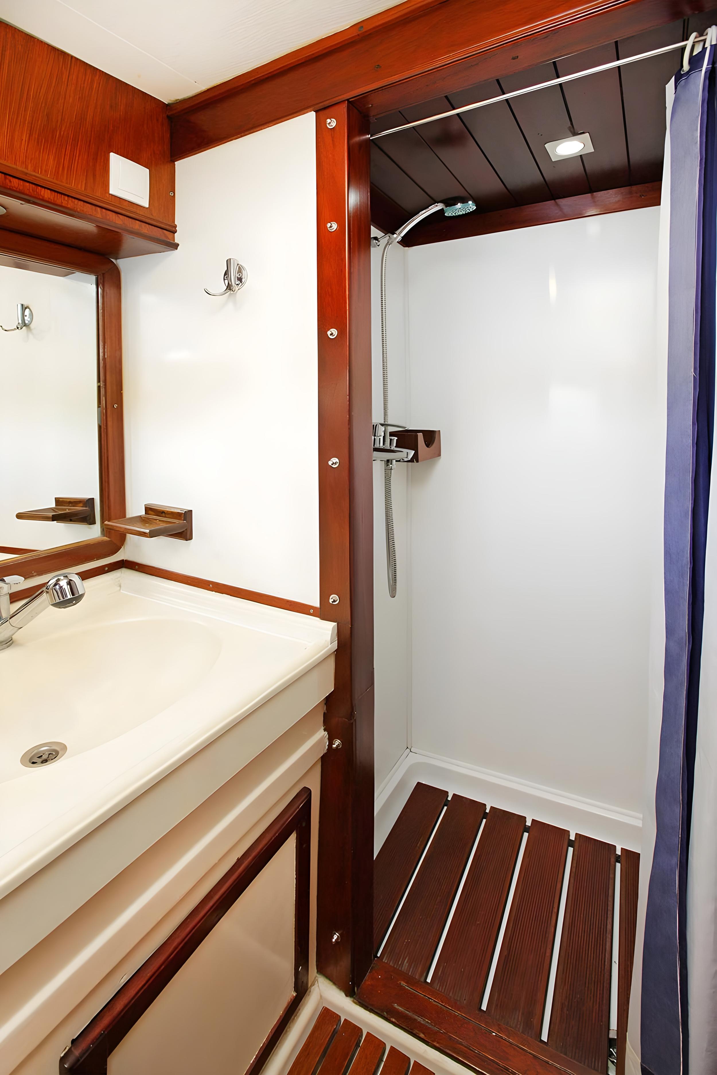 Gulet cabin bathroom with teak slatted shower floor, handheld showerhead, white vanity sink and dark wood trim