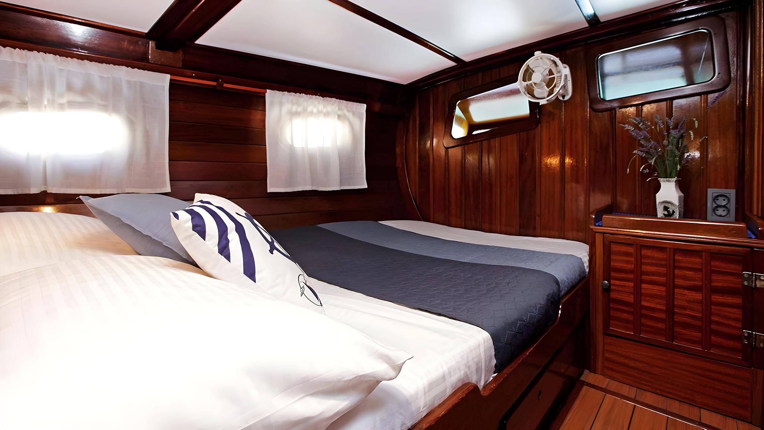 Gulet twin cabin with two single beds, dark wood panelling, portholes and wall-mounted fan