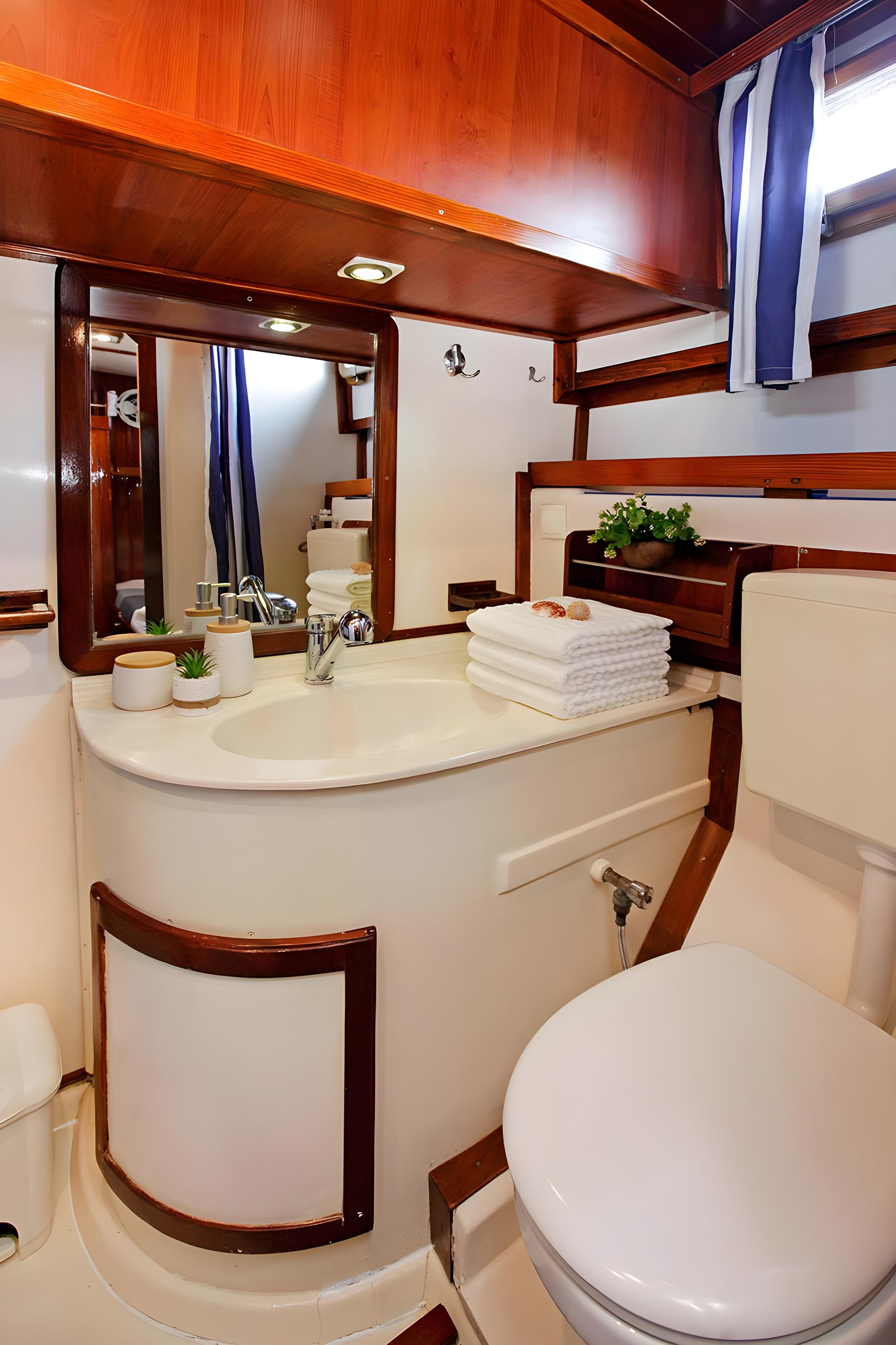 Gulet cabin bathroom with white oval vanity, chrome tap, folded white towels, and wooden trim ceiling