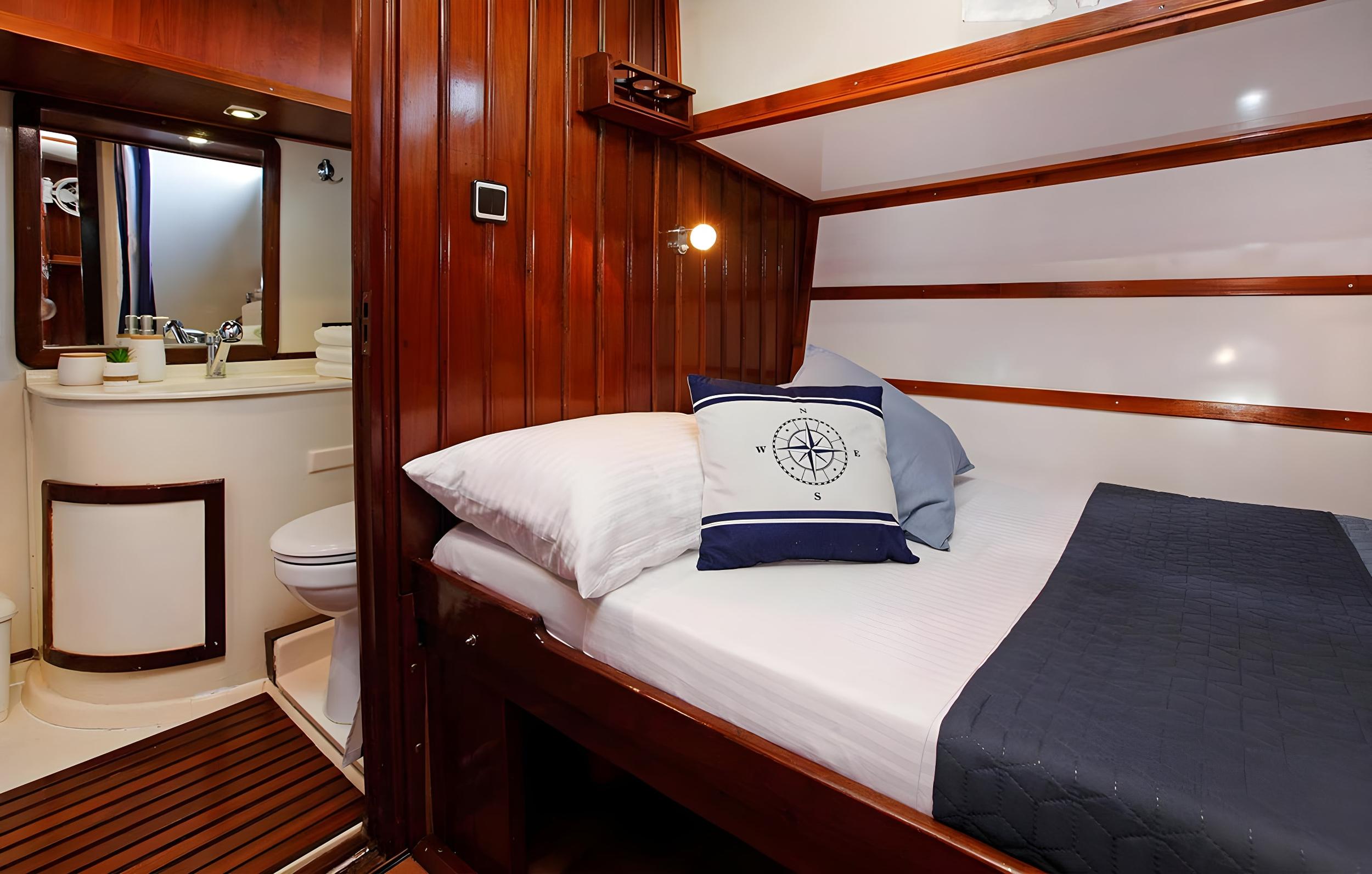 Gulet guest cabin with single bed, nautical cushions, and en-suite bathroom with sink and toilet visible