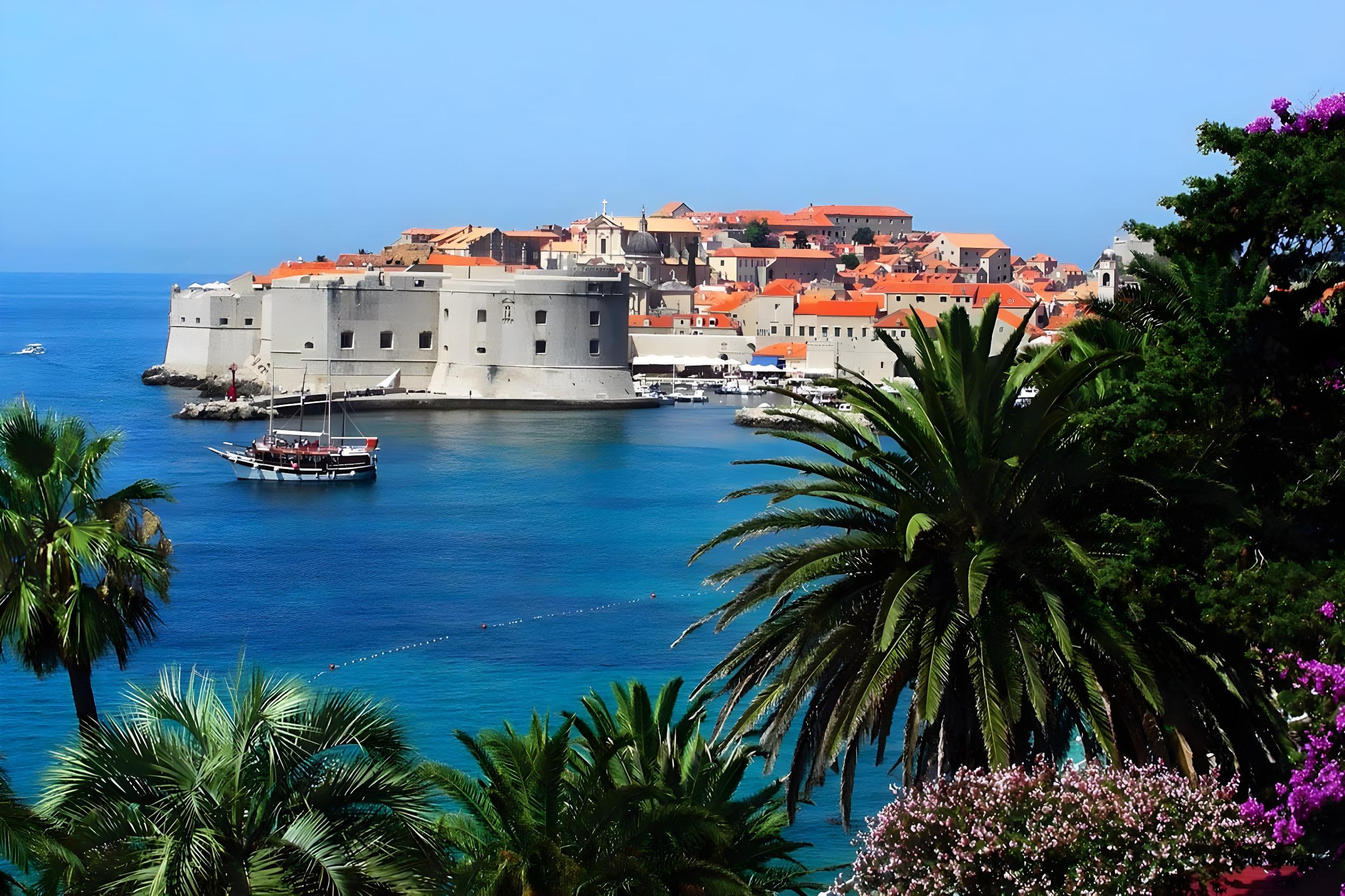 Dubrovnik old town walled city with traditional sailing gulet anchored in turquoise harbour