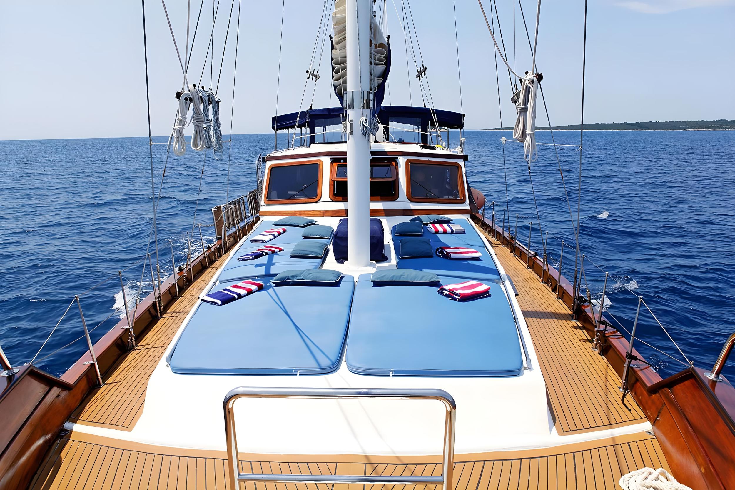 Gulet bow deck with six blue sun mattresses, green cushions and striped towels sailing open sea