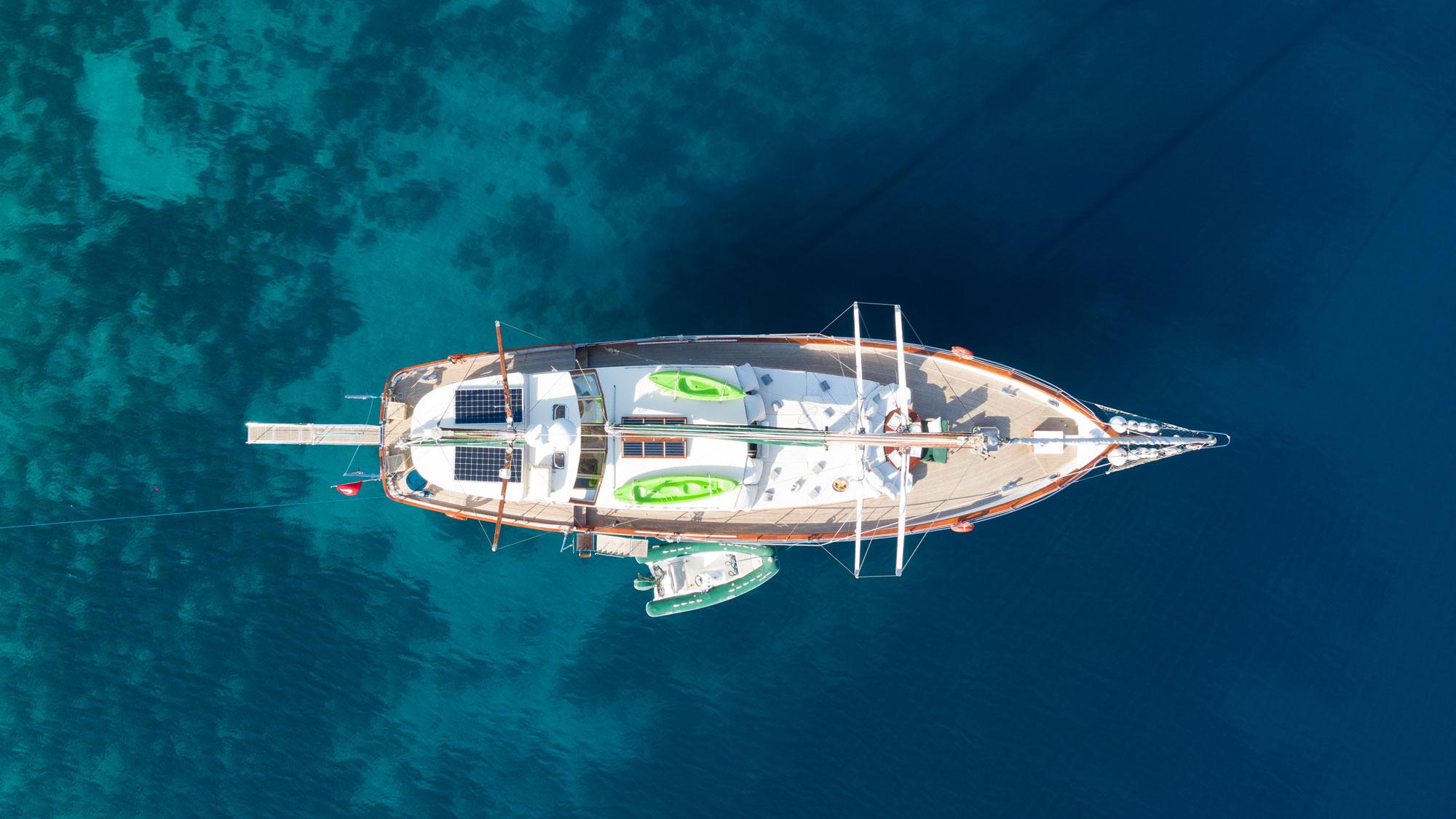 aerial view of white sailing yacht with two green kayaks on deck anchored in crystal clear blue waters