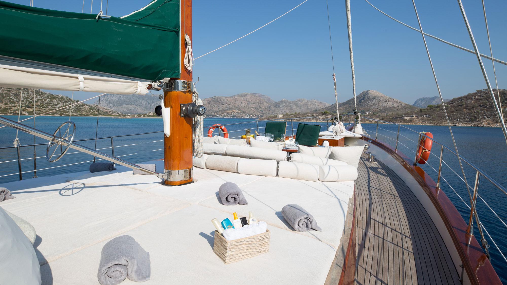 Forward deck sun loungers with white cushions, rolled towels and service basket on luxury gulet