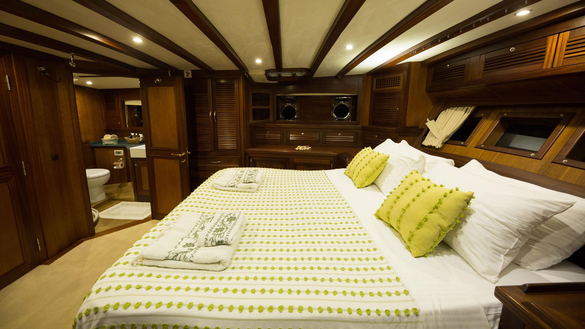 yacht cabin interior with white bedding, green polka dot throw, wood paneling and en-suite bathroom