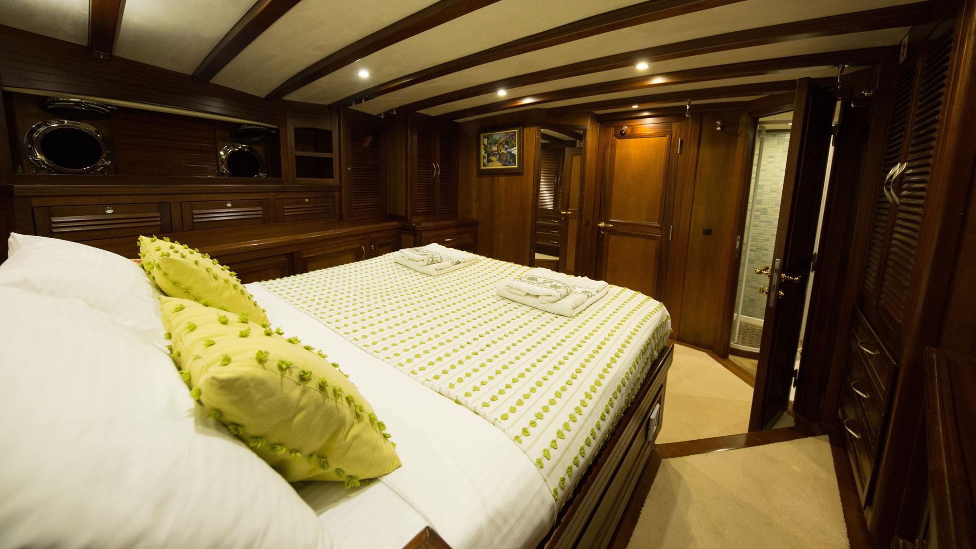 yacht guest cabin featuring double bed with green patterned bedding and dark wood paneling