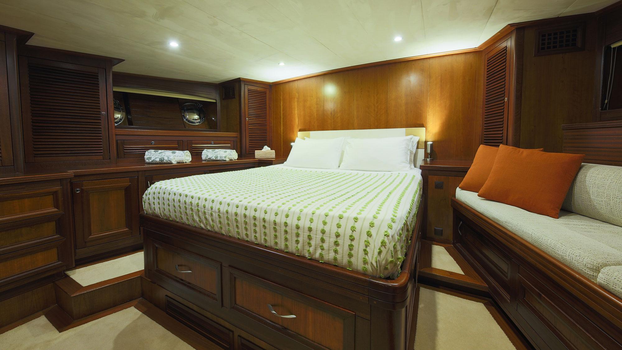 yacht guest cabin featuring double bed with green patterned bedding and built-in sofa seating