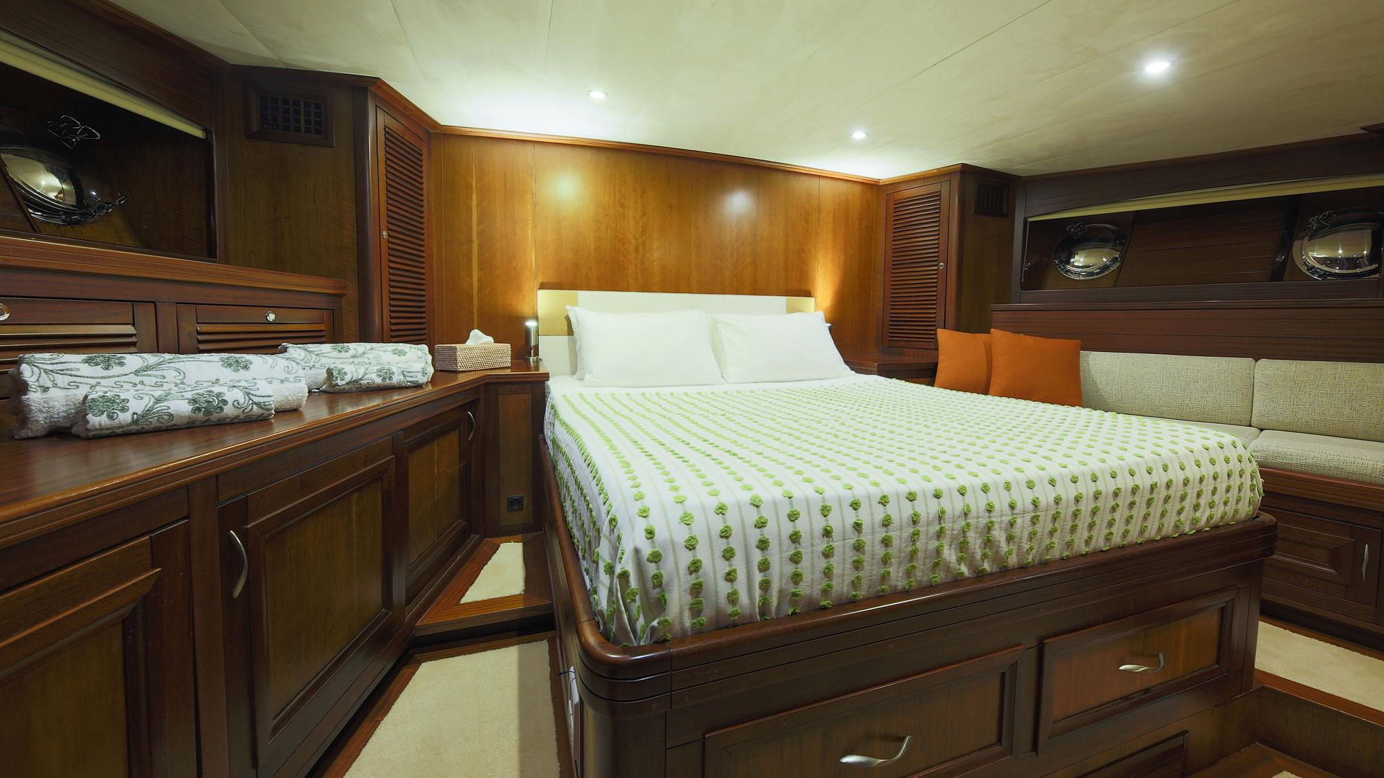 yacht cabin with double bed, green patterned bedding, wood paneling and built-in storage