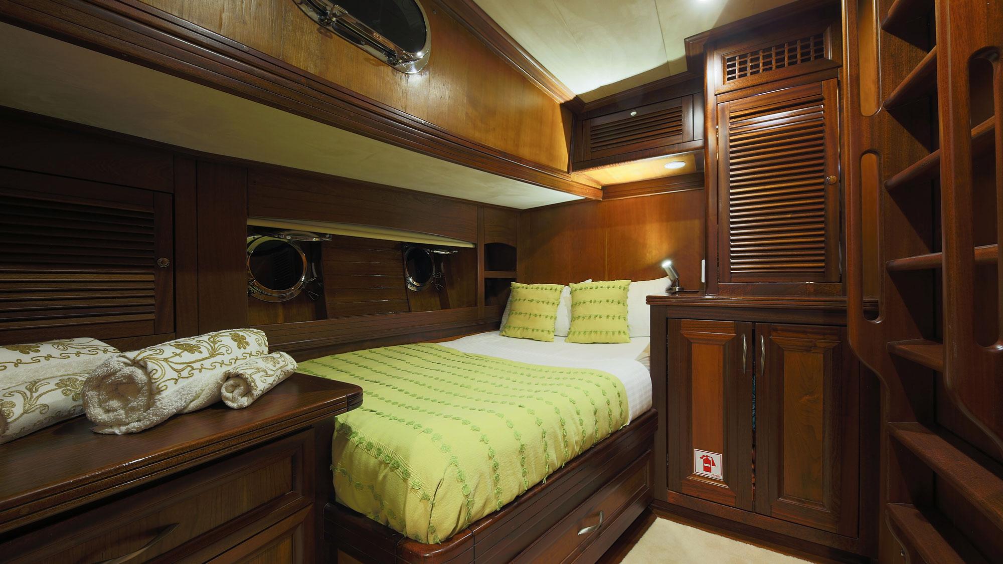 yacht guest cabin interior with double bed, green bedding, portholes, and wood cabinetry