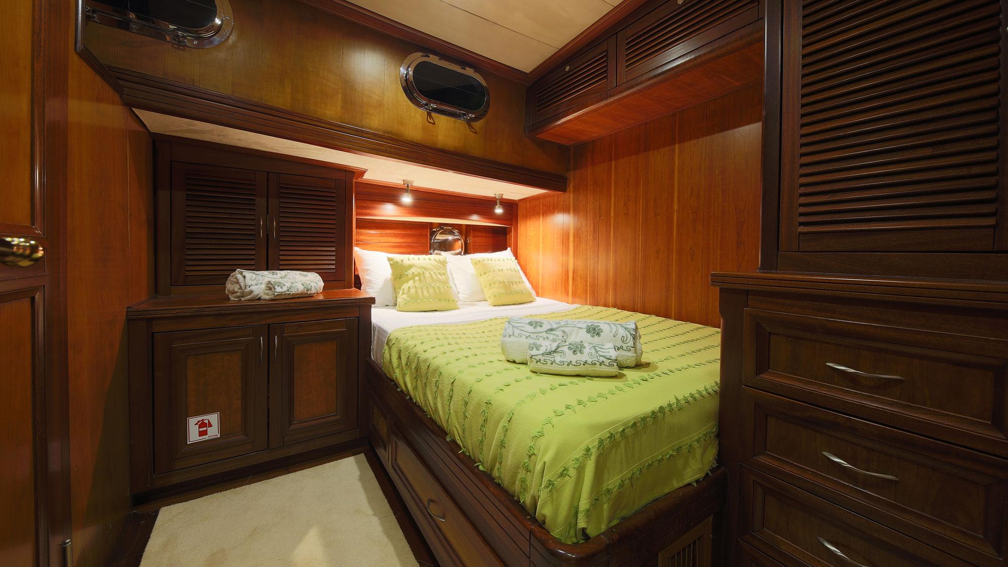 yacht guest cabin with double bed, green bedding, built-in storage and porthole window