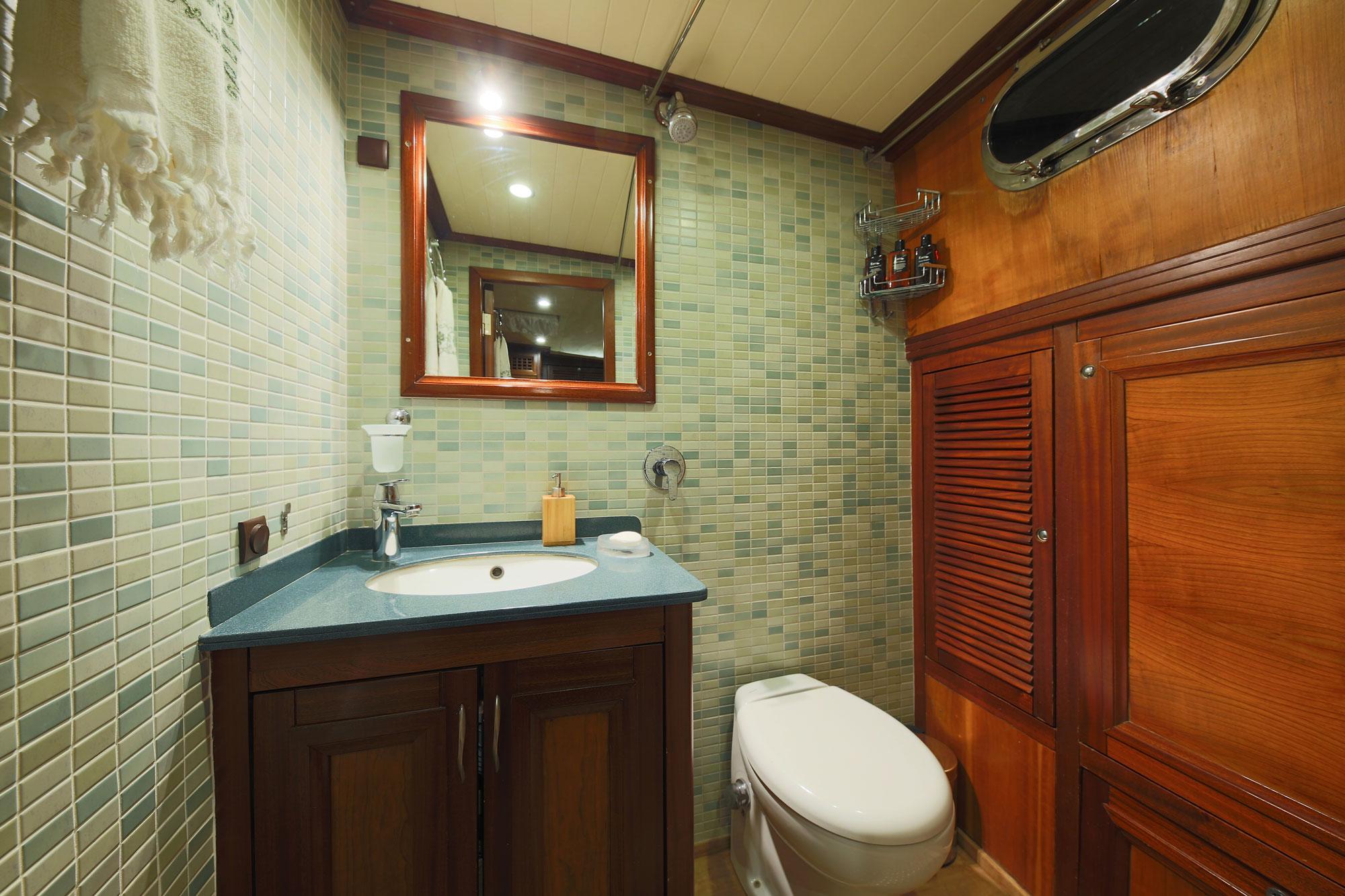 compact yacht bathroom featuring green mosaic tile walls, wooden vanity with basin, and built-in storage