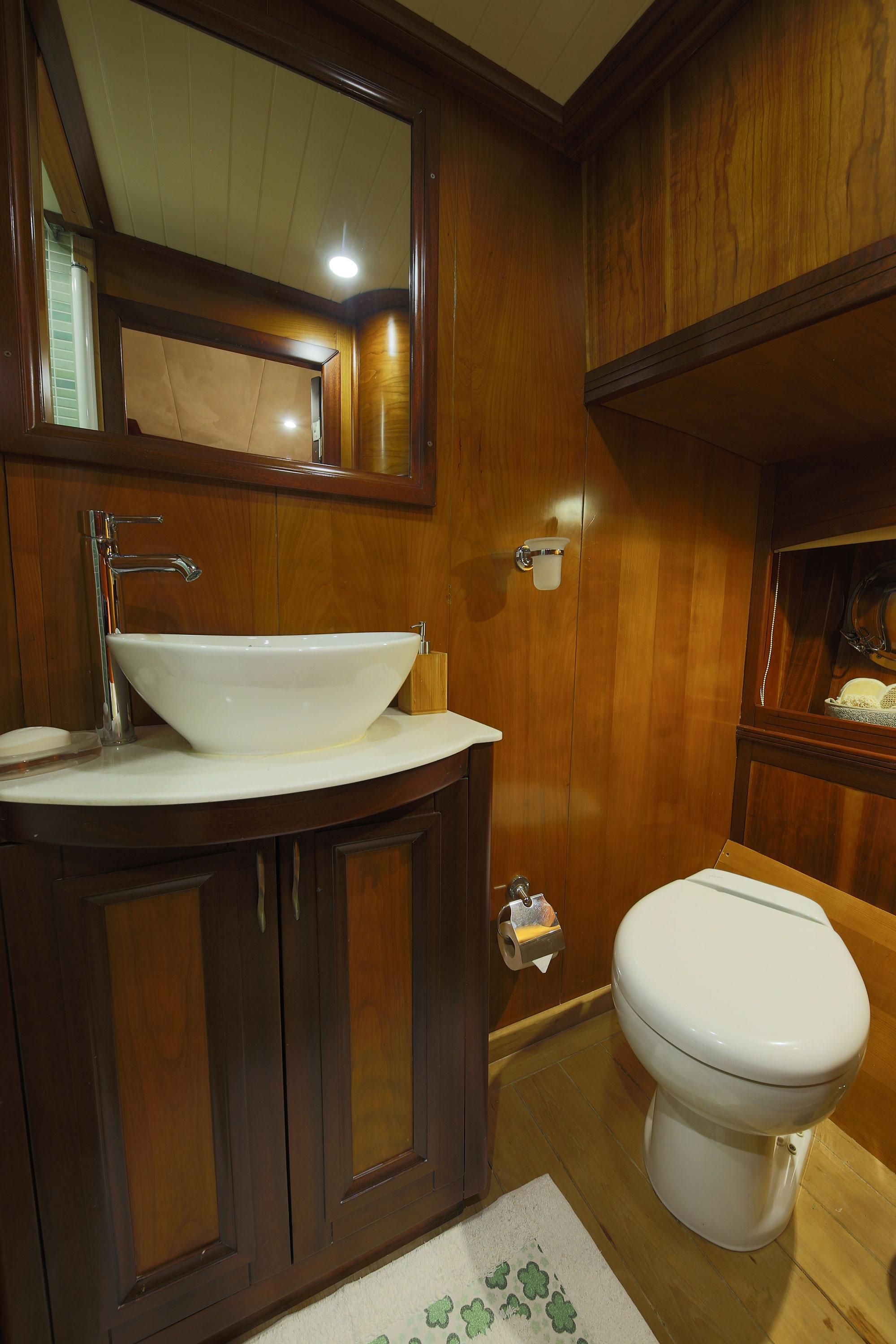 compact yacht guest bathroom with white vessel sink, wooden vanity and toilet