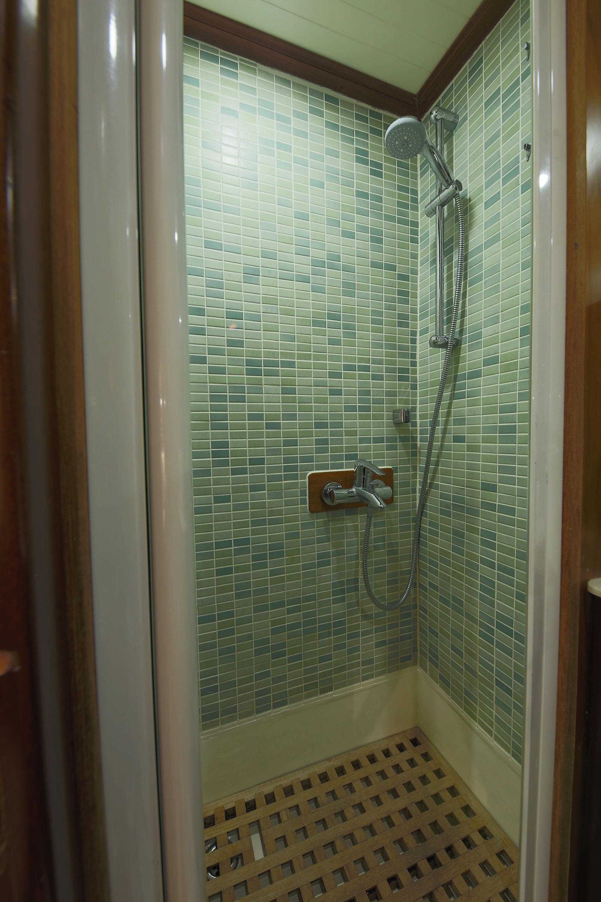 yacht bathroom shower stall with green glass mosaic tile walls and handheld shower fixture