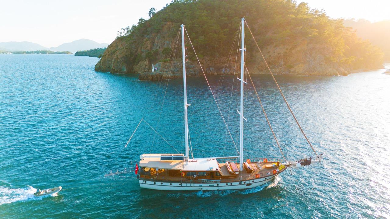 aerial view of traditional gulet yacht anchored in turquoise waters near rocky forested peninsula at golden hour