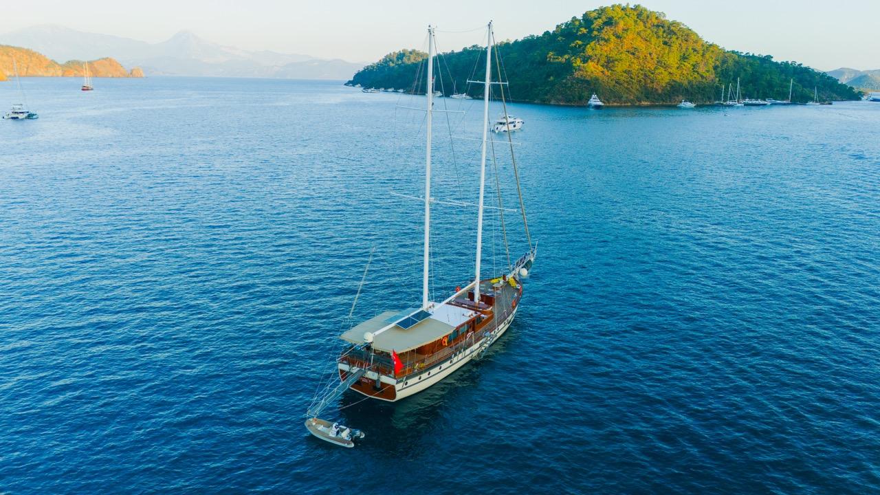 Aerial view of traditional wooden gulet yacht anchored in turquoise Mediterranean bay with forested islands