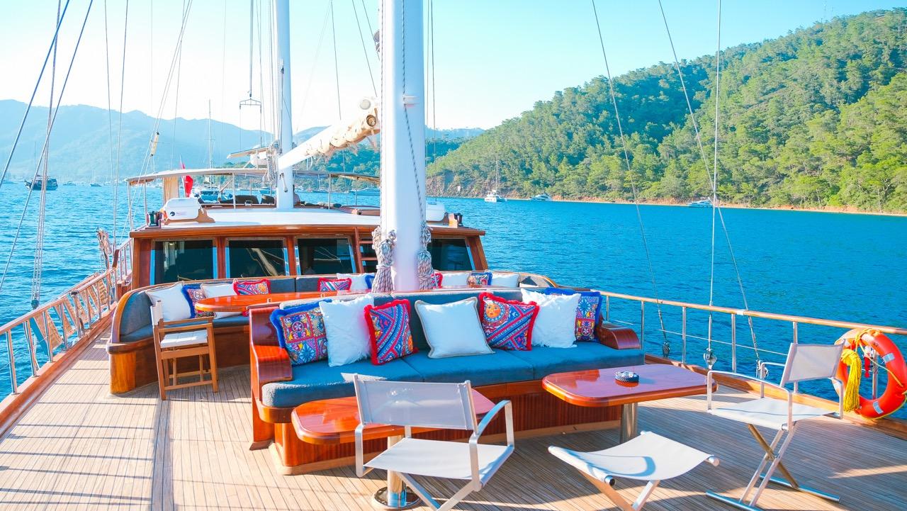 Gulet aft deck seating area with blue cushioned sofa, colorful pillows and wooden coffee table