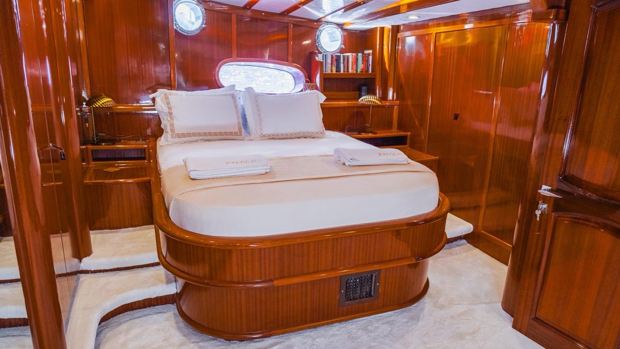 luxury yacht master cabin featuring oval bed with white linens and rich mahogany wood paneling