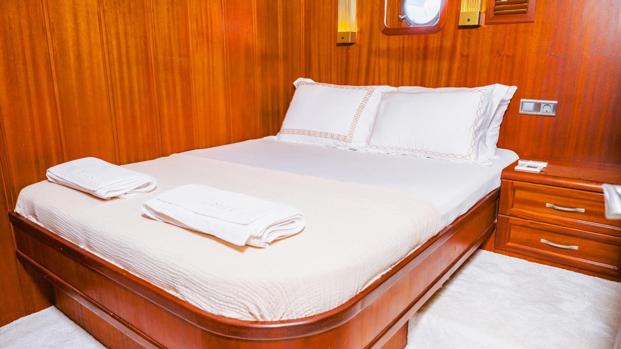 yacht guest cabin featuring double bed with white linens and rich wood paneling