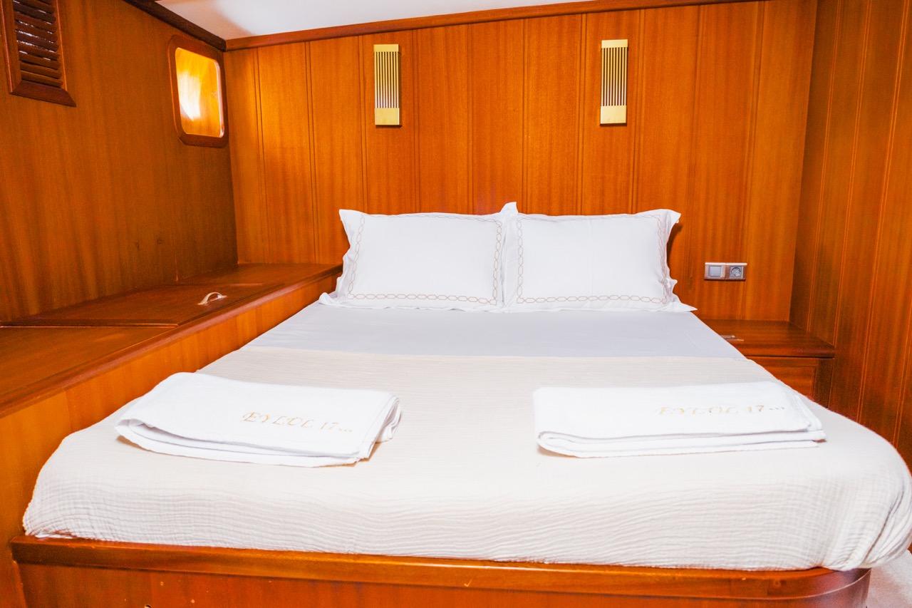 yacht guest cabin featuring double bed with white linens and rich wood paneling throughout