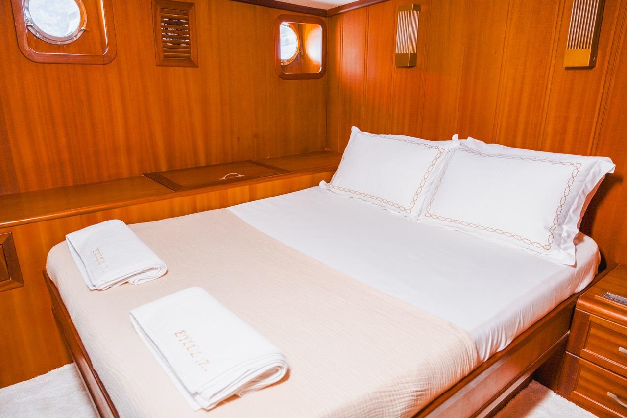 yacht cabin interior featuring double bed with white linens and warm wood paneling