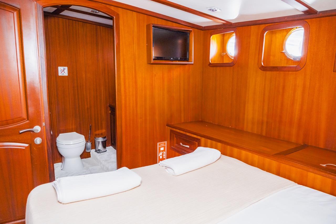 guest cabin interior with double bed, flat screen TV, portholes and ensuite bathroom door open