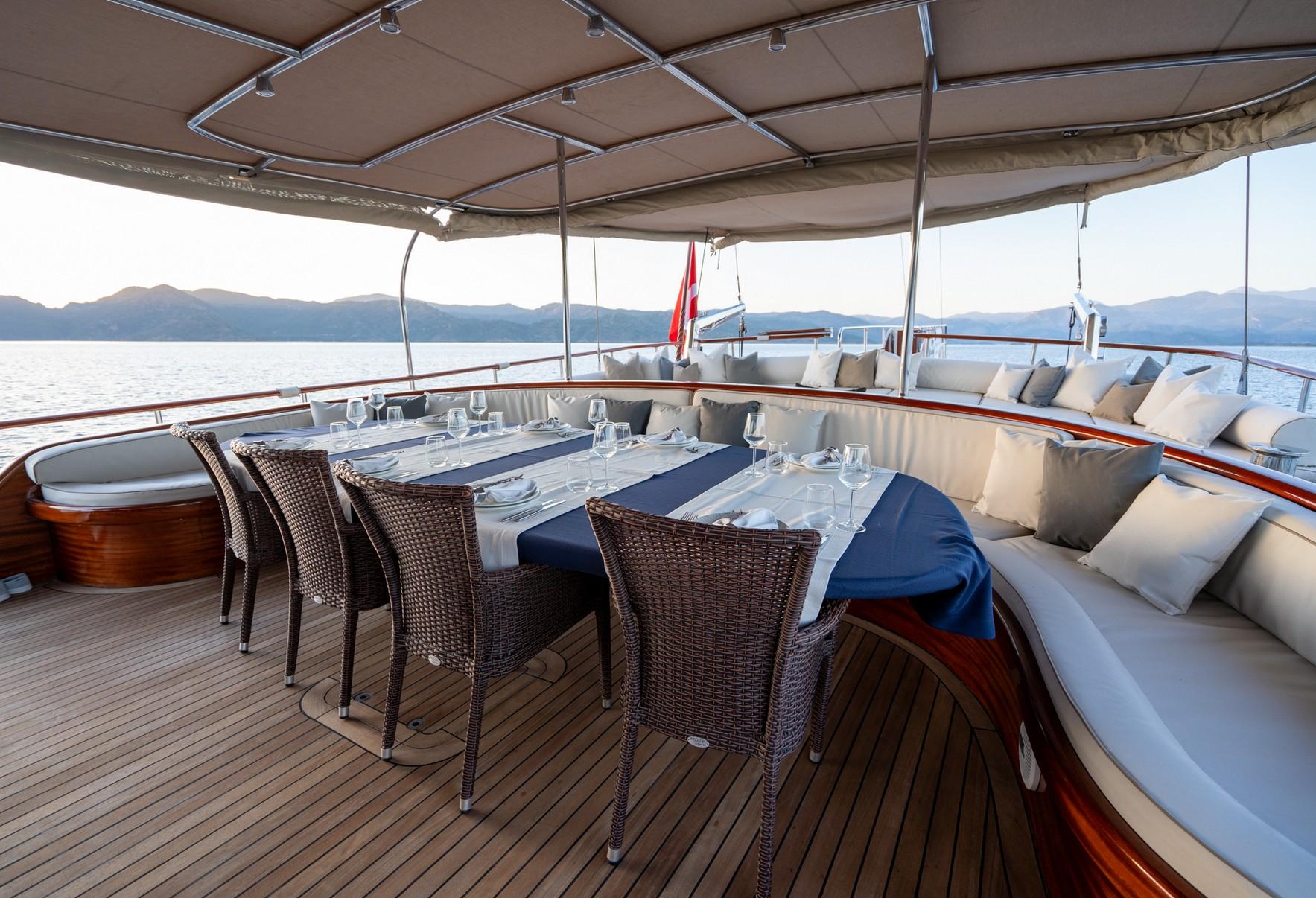 yacht aft deck dining area with wicker chairs, formal table setting under beige awning