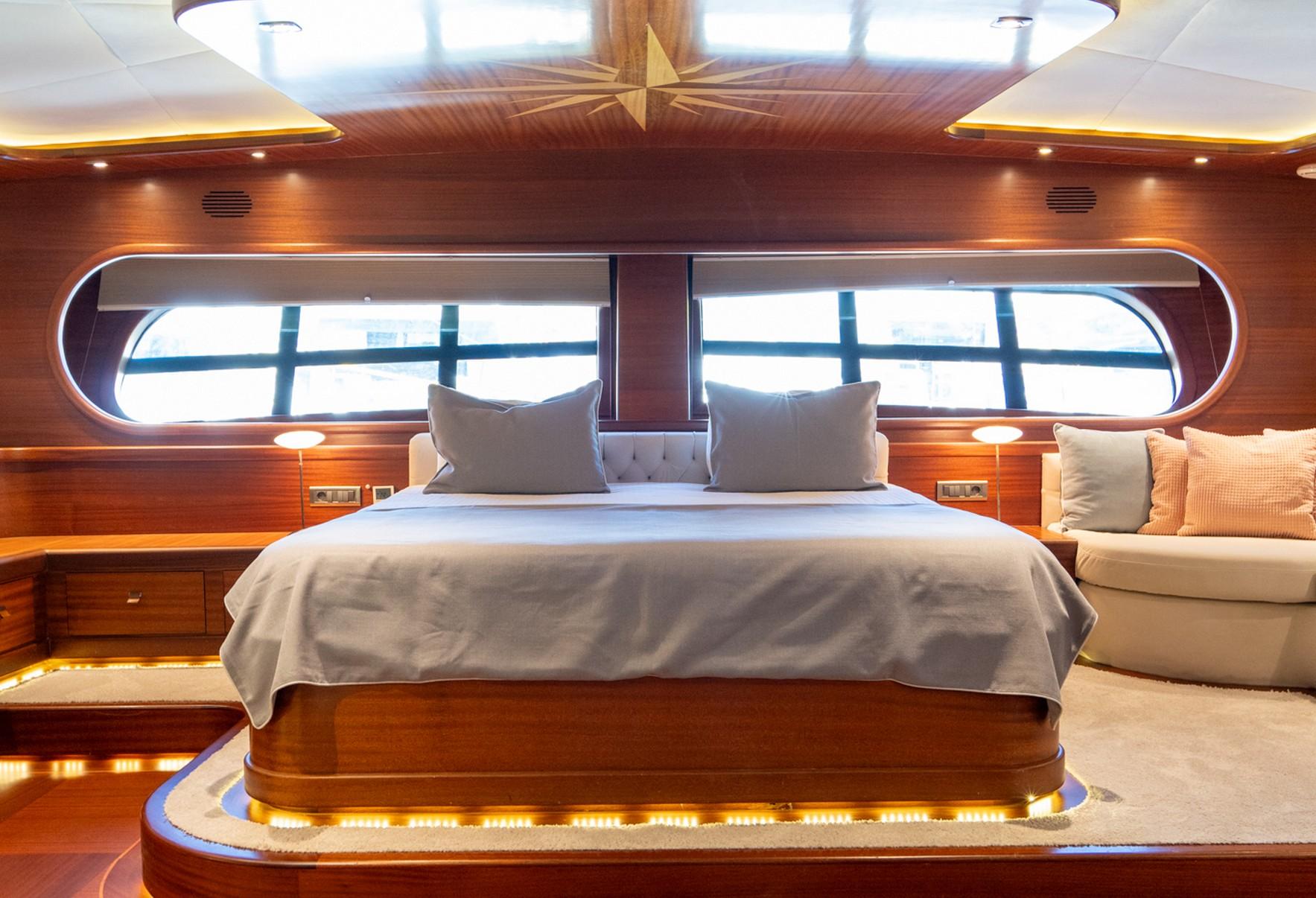 Master cabin featuring king bed with grey bedding, panoramic oval windows, warm wood paneling and LED lighting