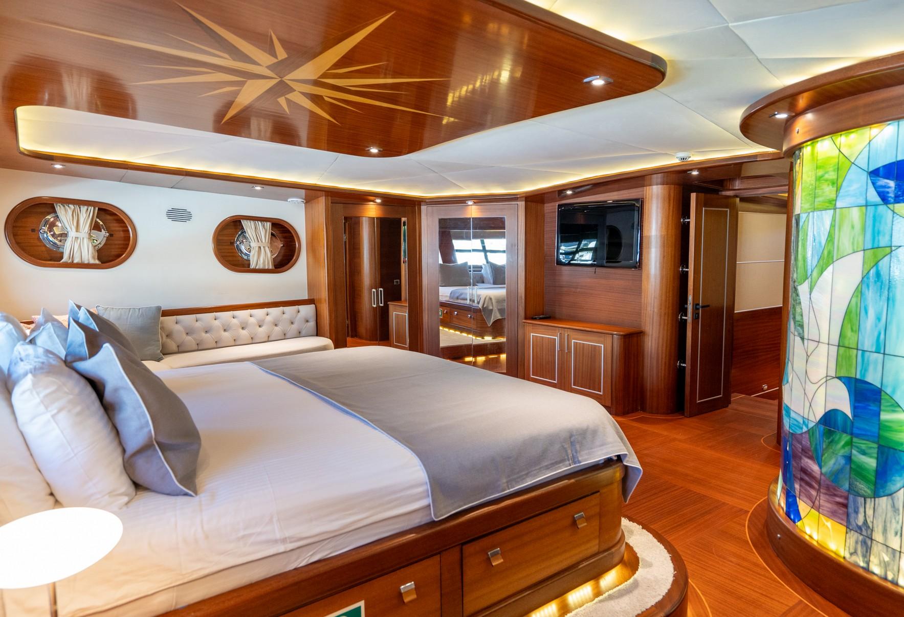 Master cabin featuring king bed, tufted headboard, entertainment center, and oval portholes