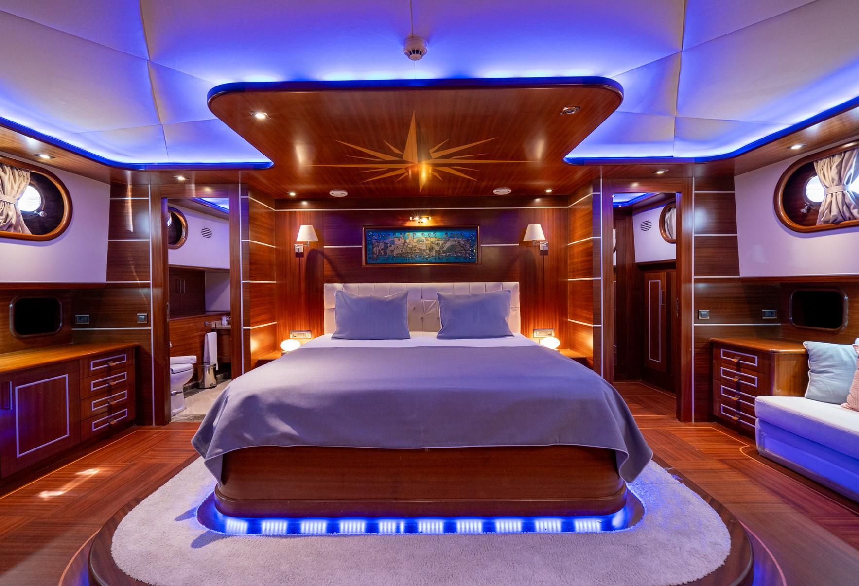 Luxury yacht master cabin featuring king bed, wood paneling, nautical star ceiling detail and blue LED lighting