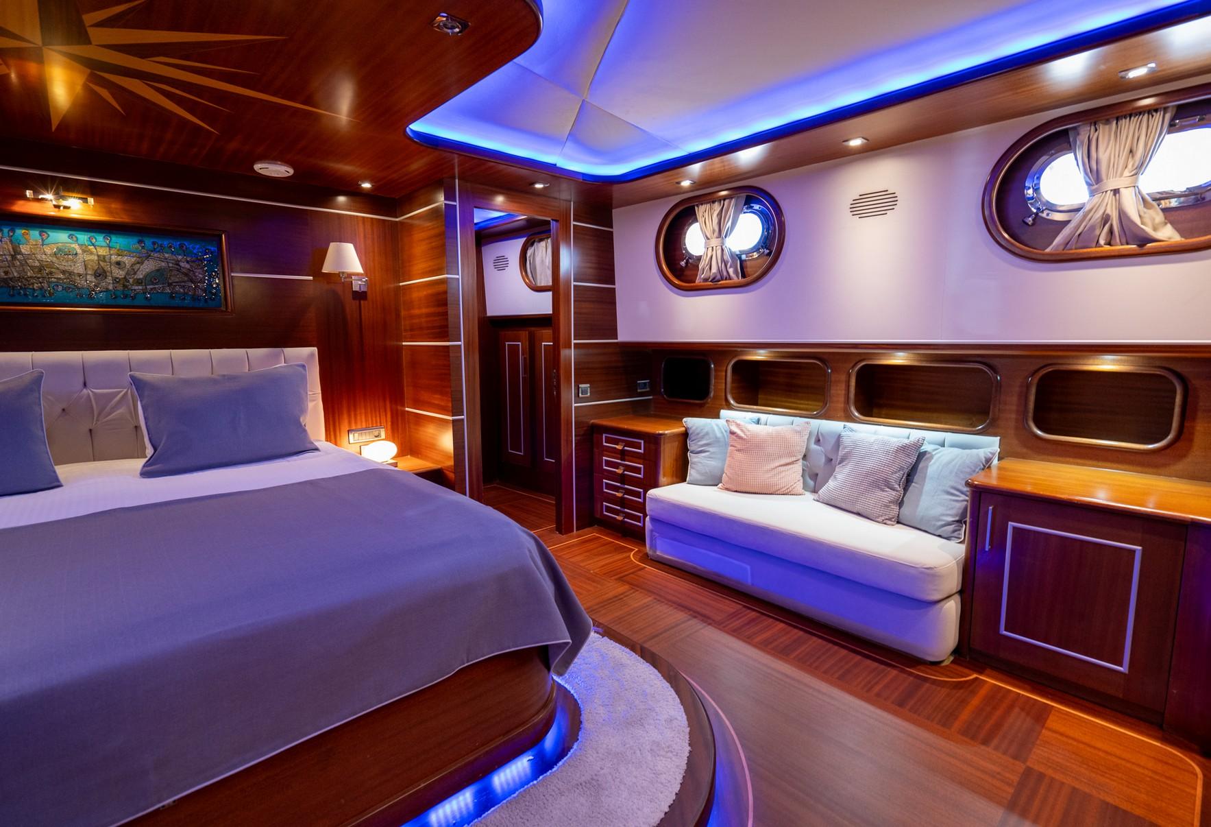 Master cabin interior with double bed, white sofa, portholes and ambient lighting