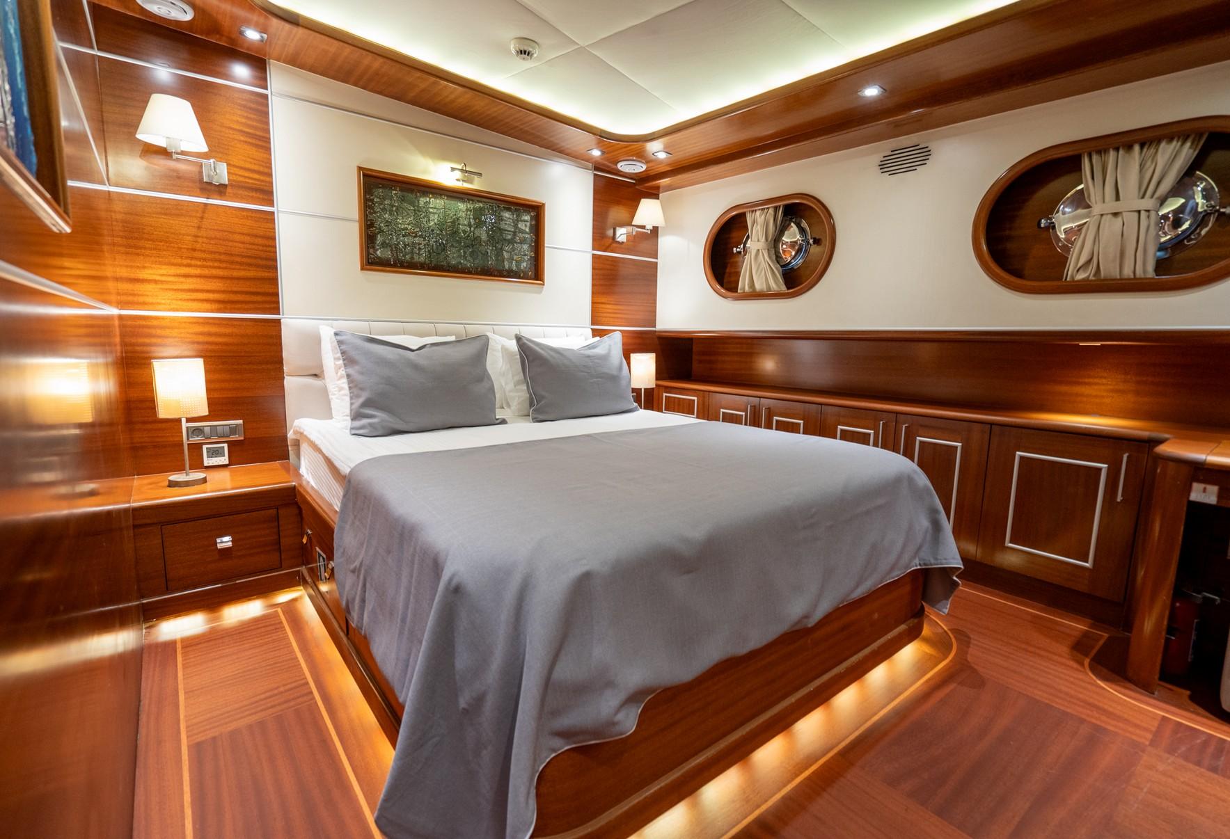 Luxury yacht cabin with double bed, wood paneling, built-in storage and oval portholes