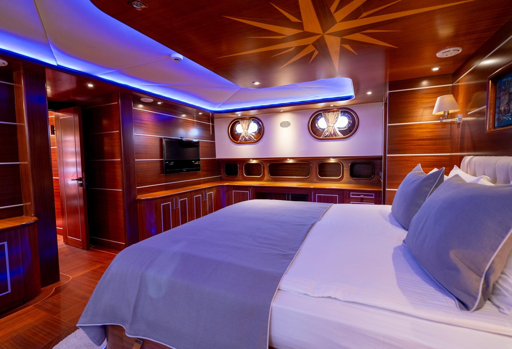 yacht cabin interior with white bedding, wall-mounted TV, wooden paneling and portholes
