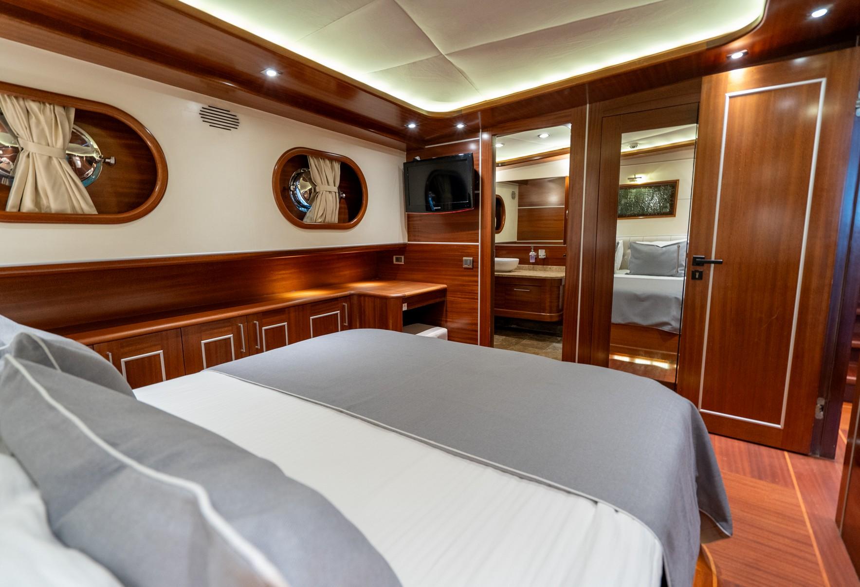 yacht cabin interior with double bed, rich wood paneling, oval portholes and en-suite bathroom entrance