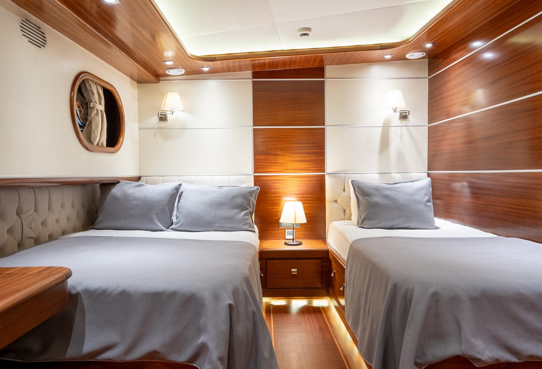 Twin guest cabin with two single beds, wood paneling, and porthole window