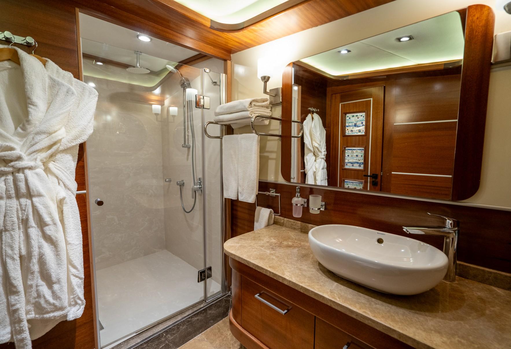 luxury yacht cabin bathroom with glass shower, oval basin, marble vanity and towel storage