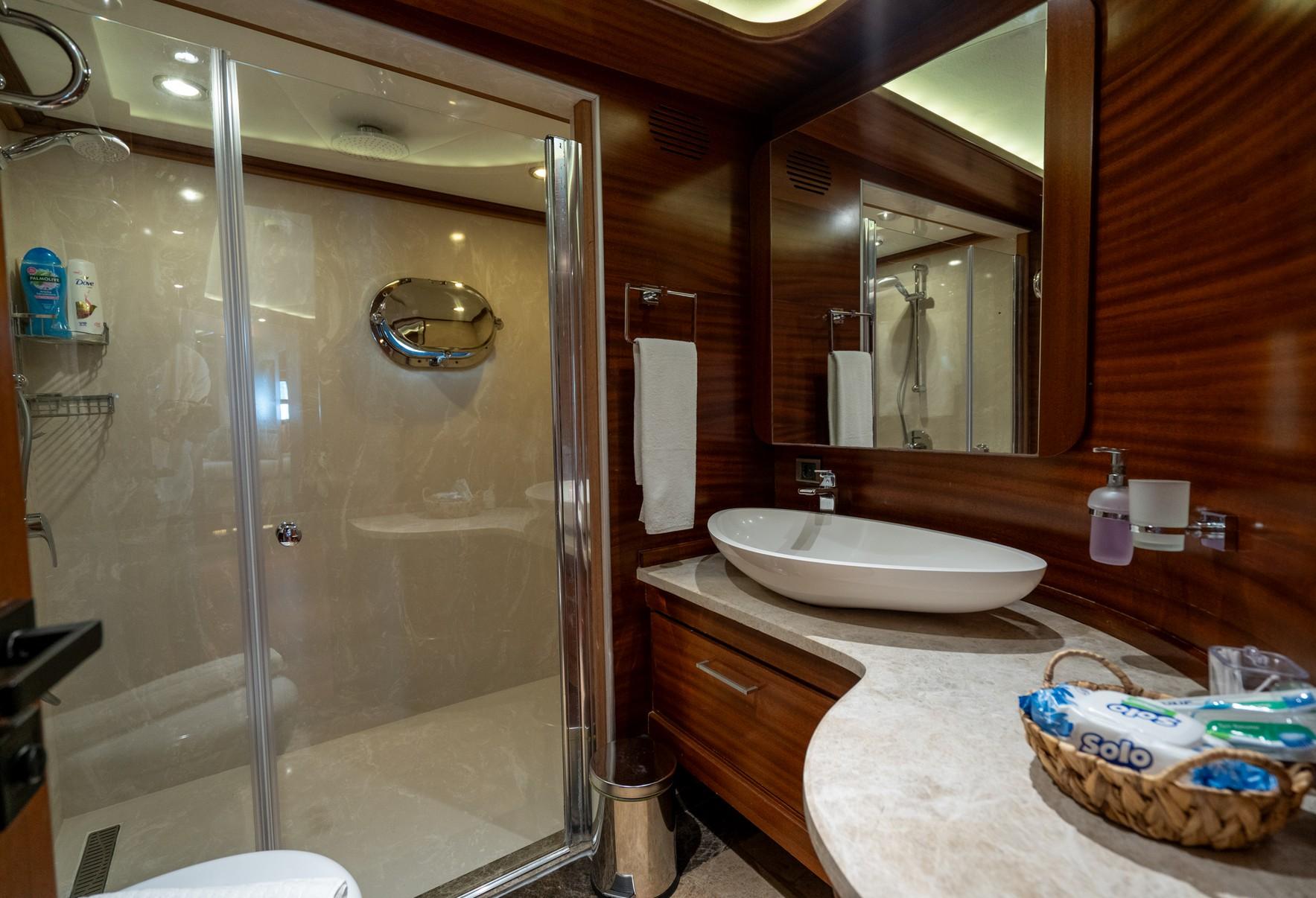 yacht bathroom featuring glass shower enclosure, marble vanity with oval basin and wooden cabinetry